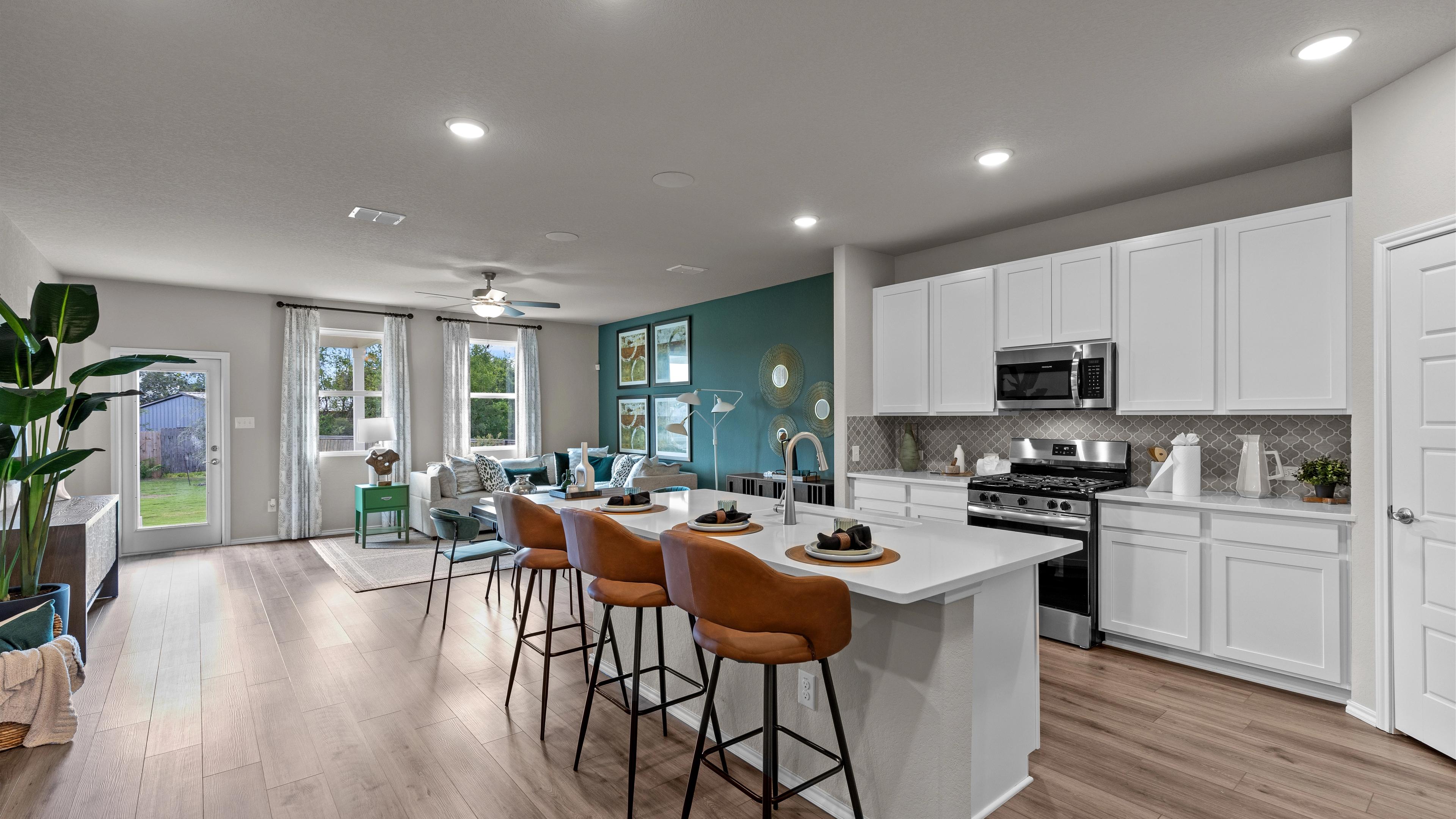 Open-concept kitchen and living area in Comanche Ridge San Antonio home by Davidson Homes with white cabinets, island bar, hardwood floors