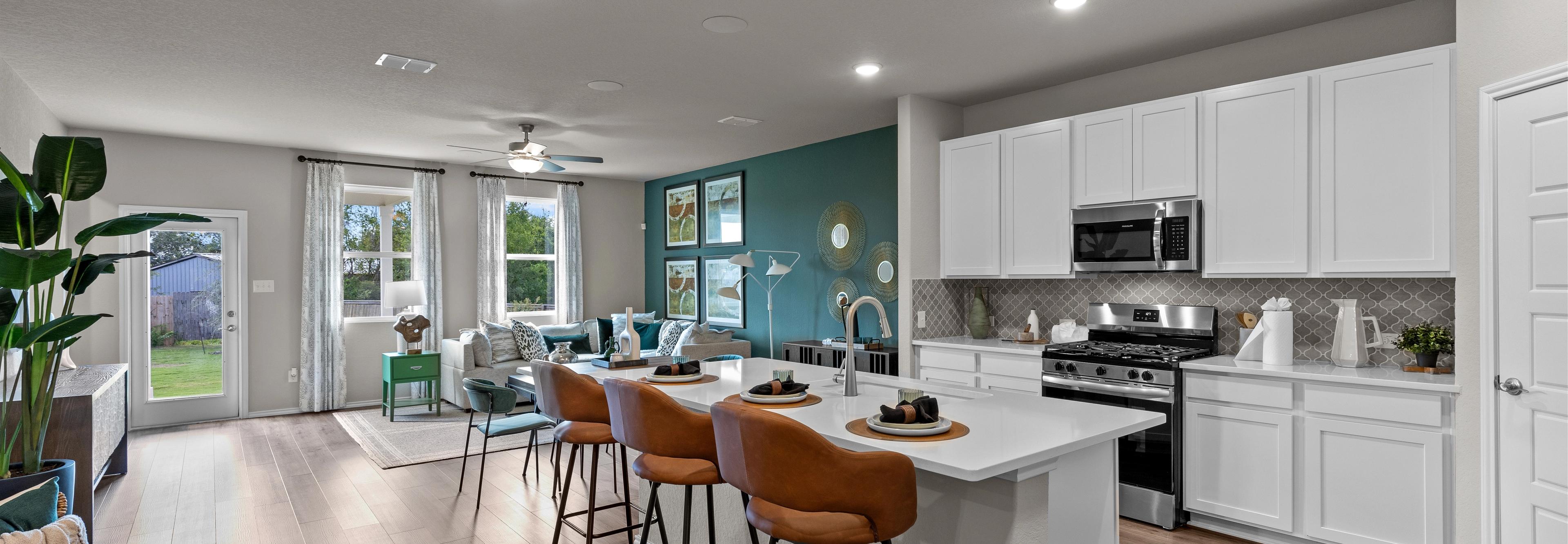 Open-concept kitchen and living area in Comanche Ridge San Antonio home by Davidson Homes with white cabinets, island bar, hardwood floors