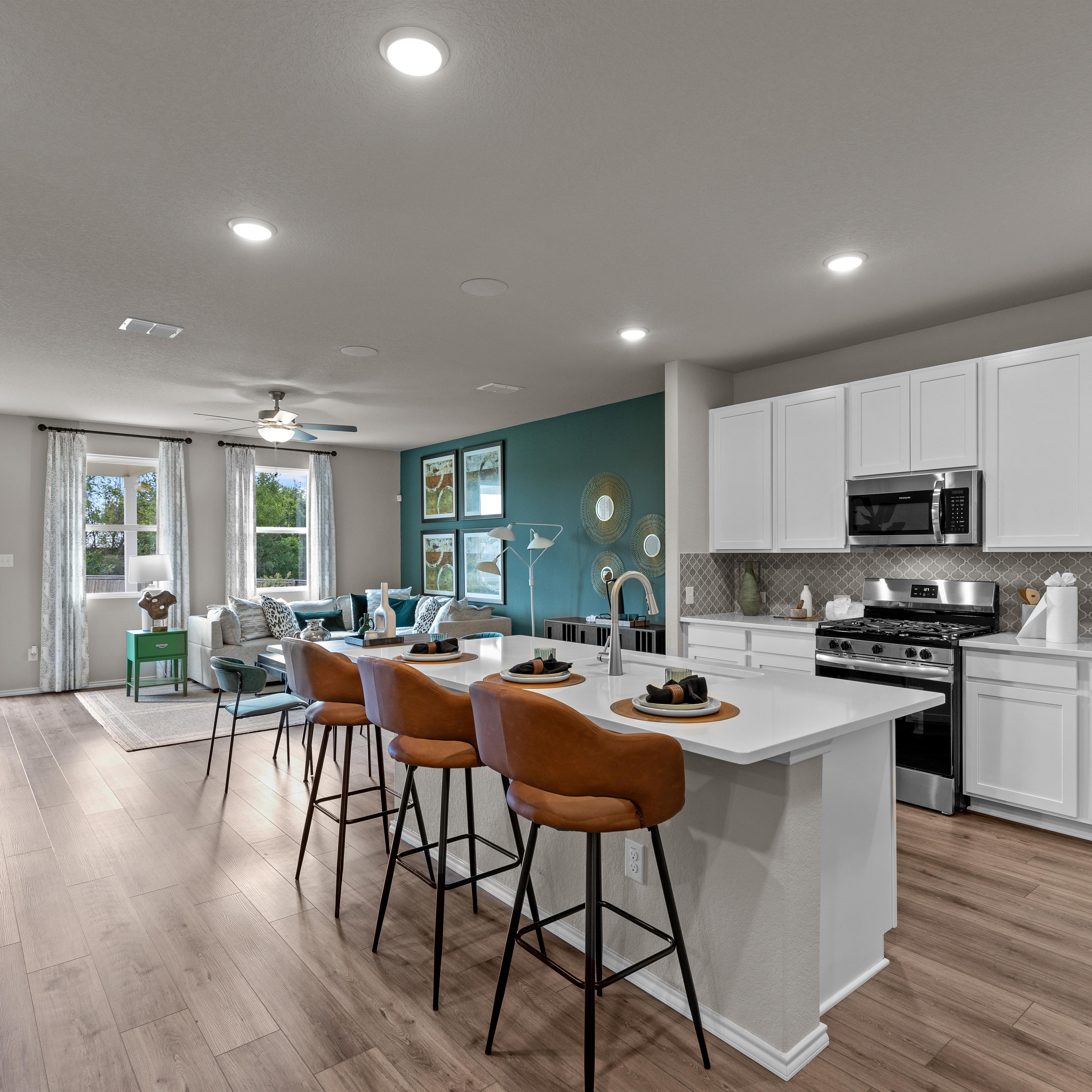Open-concept kitchen and living area in Comanche Ridge San Antonio home by Davidson Homes with white cabinets, island bar, hardwood floors