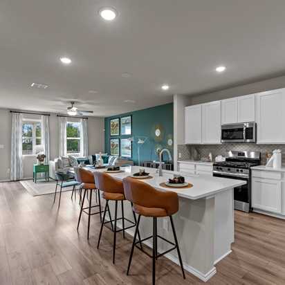 Open-concept kitchen and living area in Comanche Ridge San Antonio home by Davidson Homes with white cabinets, island bar, hardwood floors