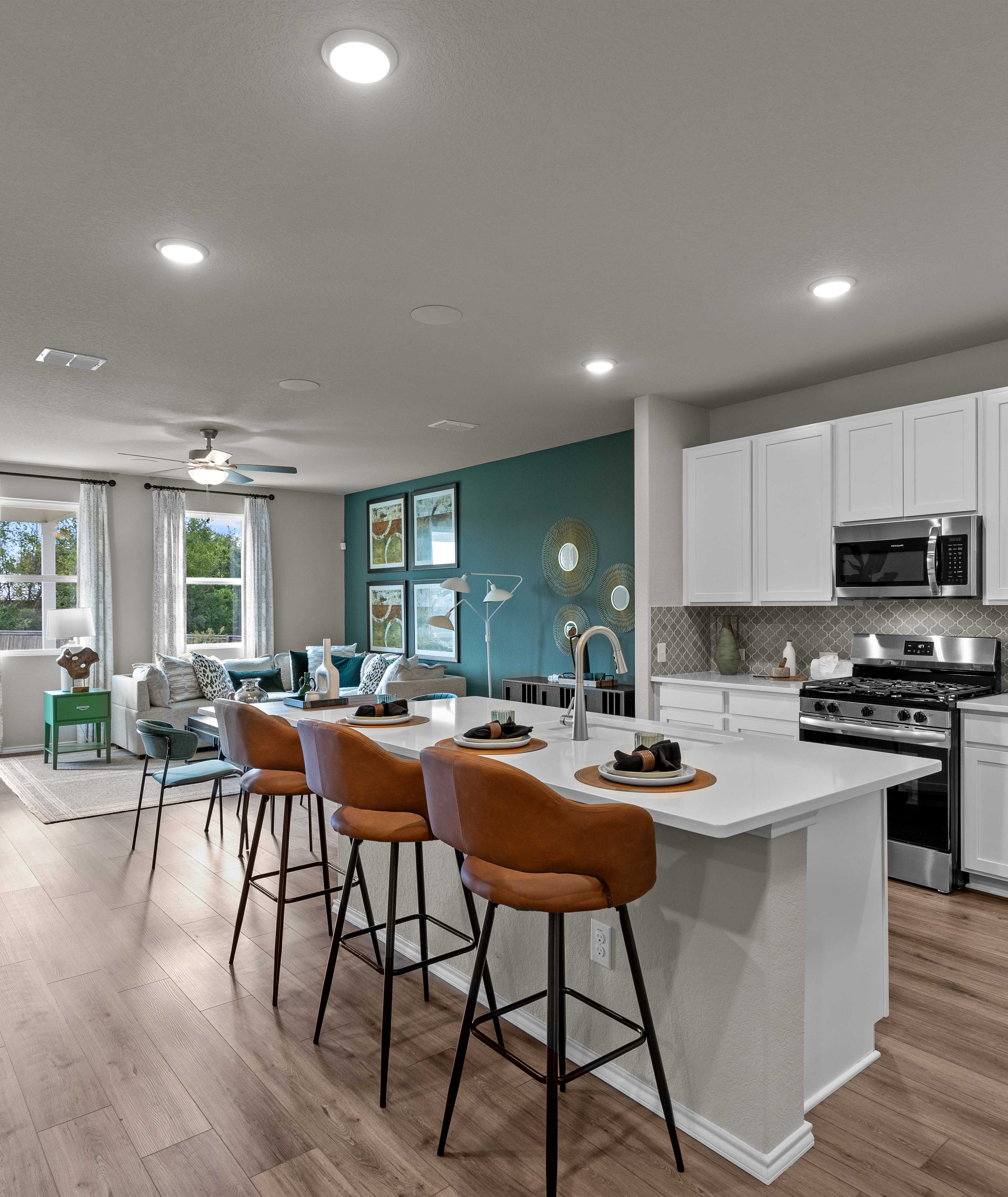 Open-concept kitchen and living area in Comanche Ridge San Antonio home by Davidson Homes with white cabinets, island bar, hardwood floors