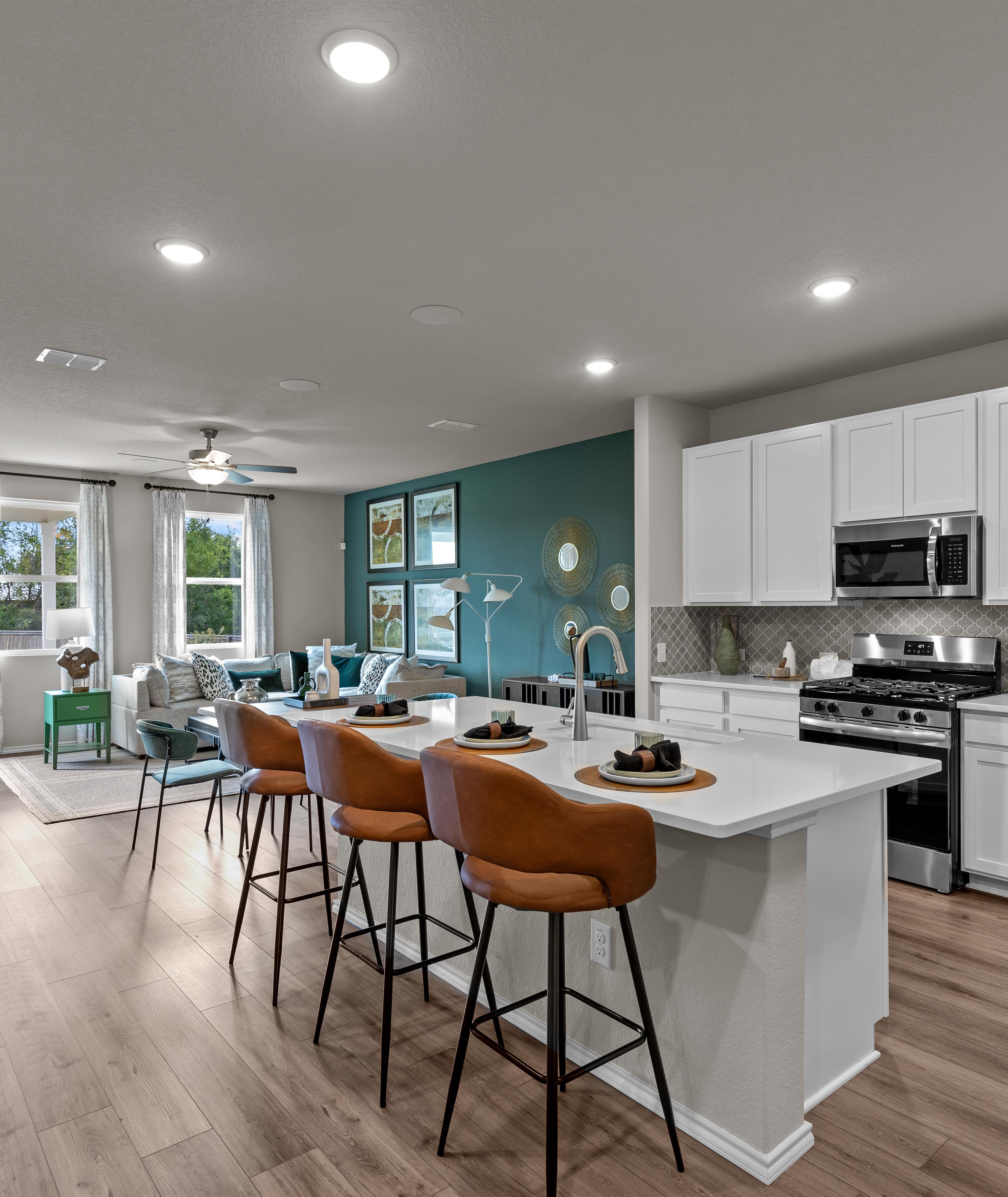 Open-concept kitchen and living area in Comanche Ridge San Antonio home by Davidson Homes with white cabinets, island bar, hardwood floors