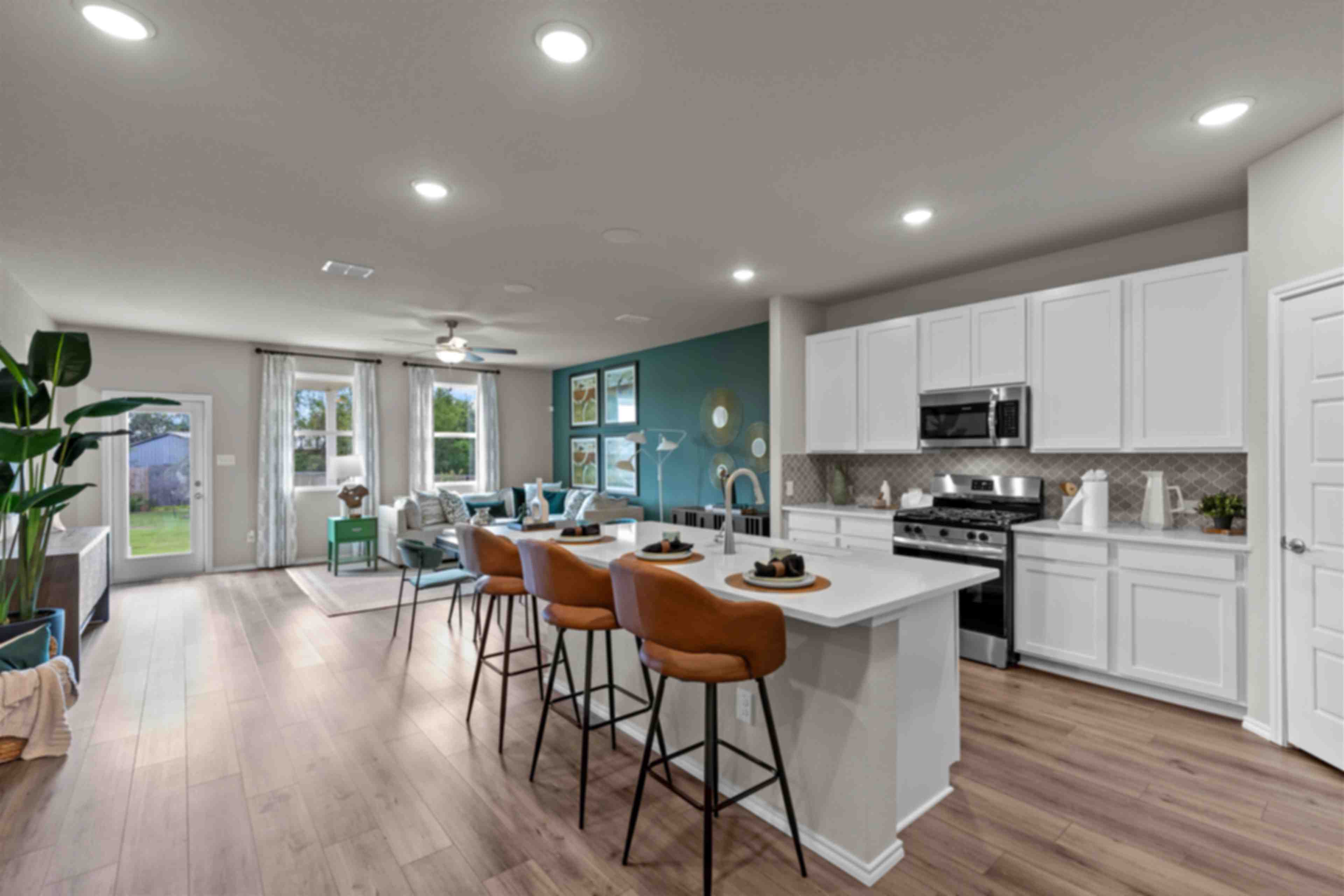 Open-concept kitchen and living area in Comanche Ridge San Antonio home by Davidson Homes with white cabinets, island bar, hardwood floors