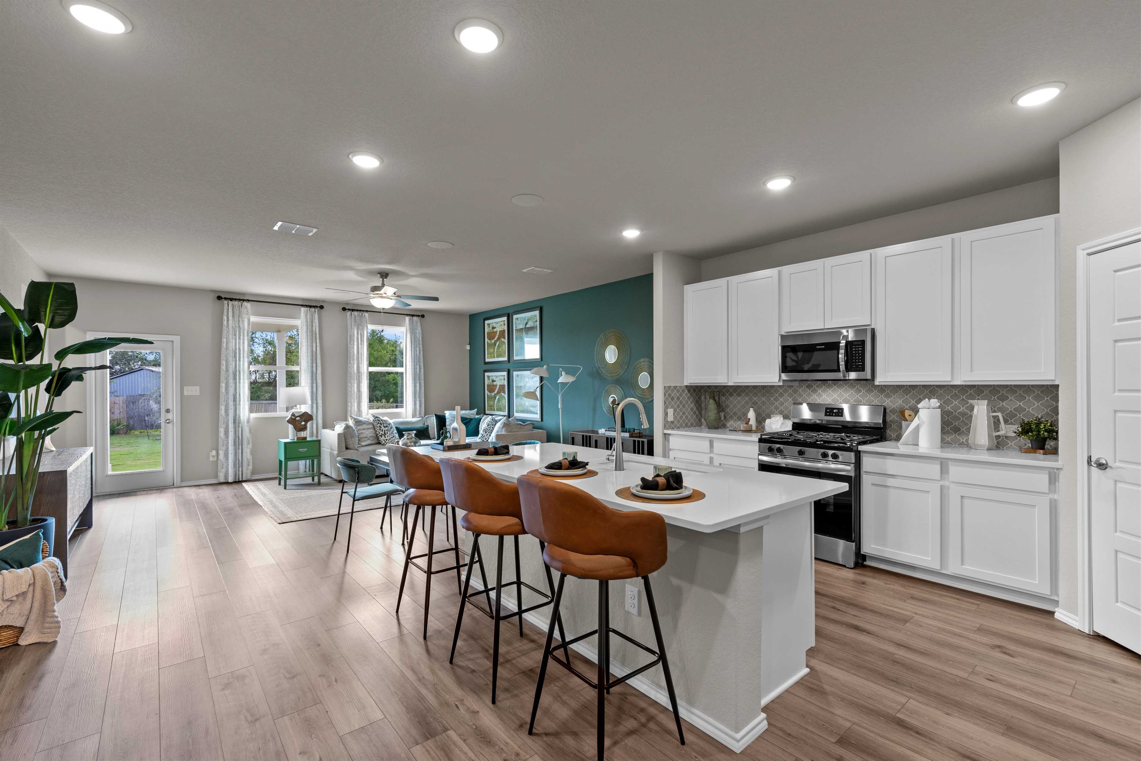 Open-concept kitchen and living room in Comanche Ridge, San Antonio TX by Davidson Homes with white island, orange barstools, hardwood floors