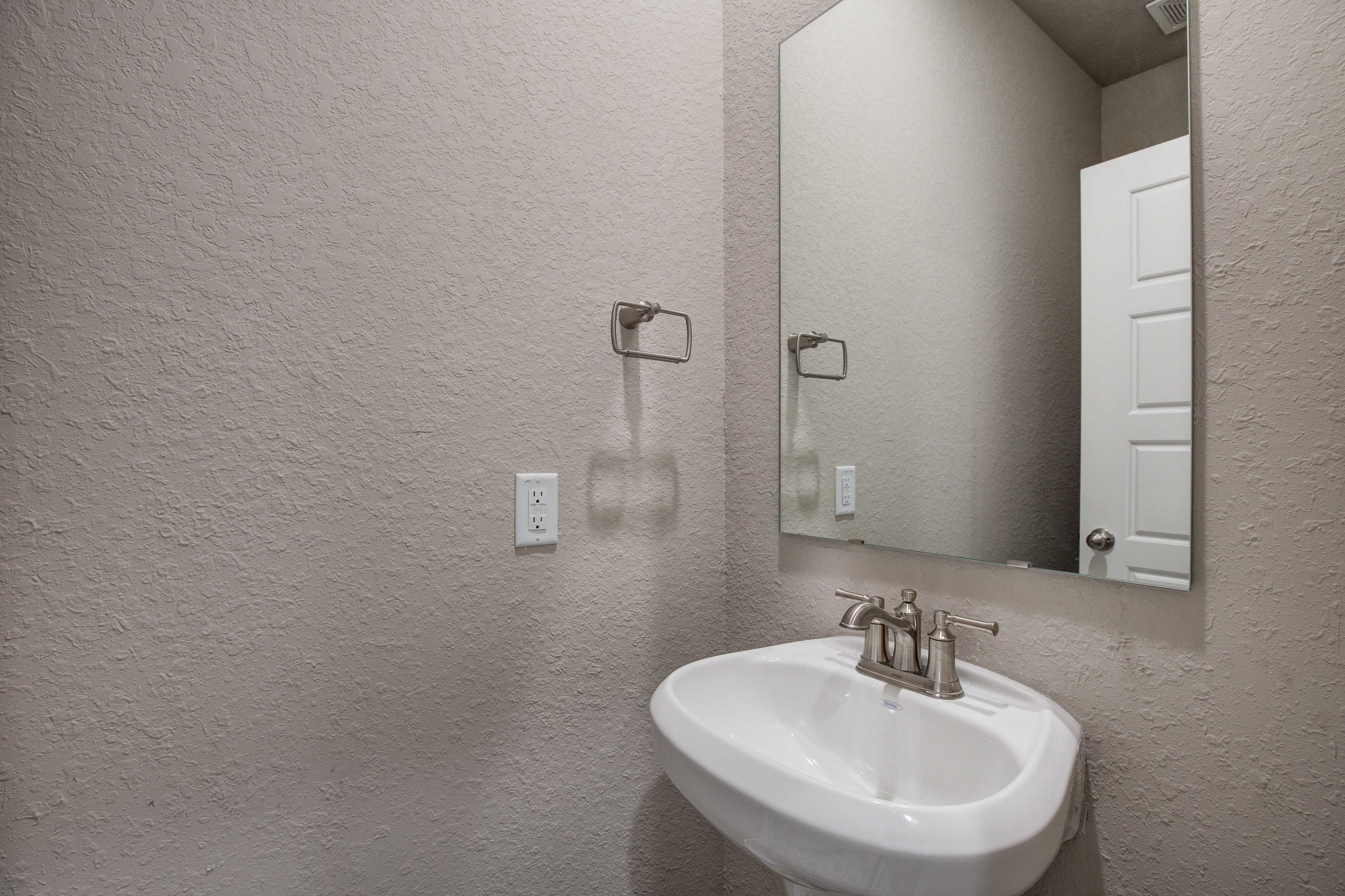 Modern bathroom vanity in The Murray home by Davidson Homes with white pedestal sink, chrome faucet, and large mirror on beige walls