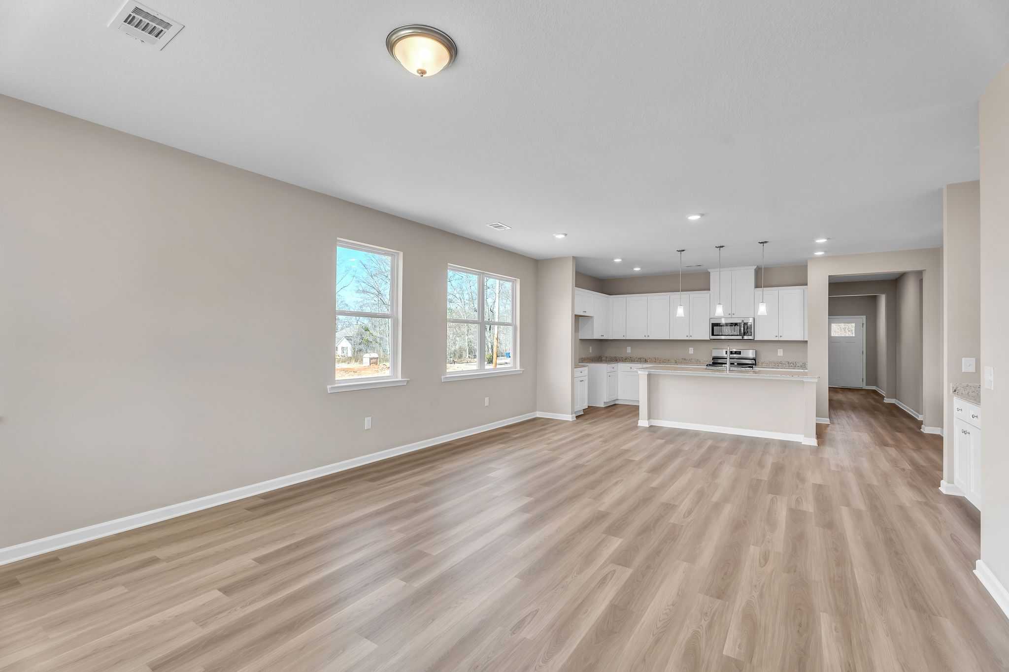 Spacious open-concept kitchen at Anderson Lakes in Opelika Alabama with white cabinets, light wood floors, and large windows