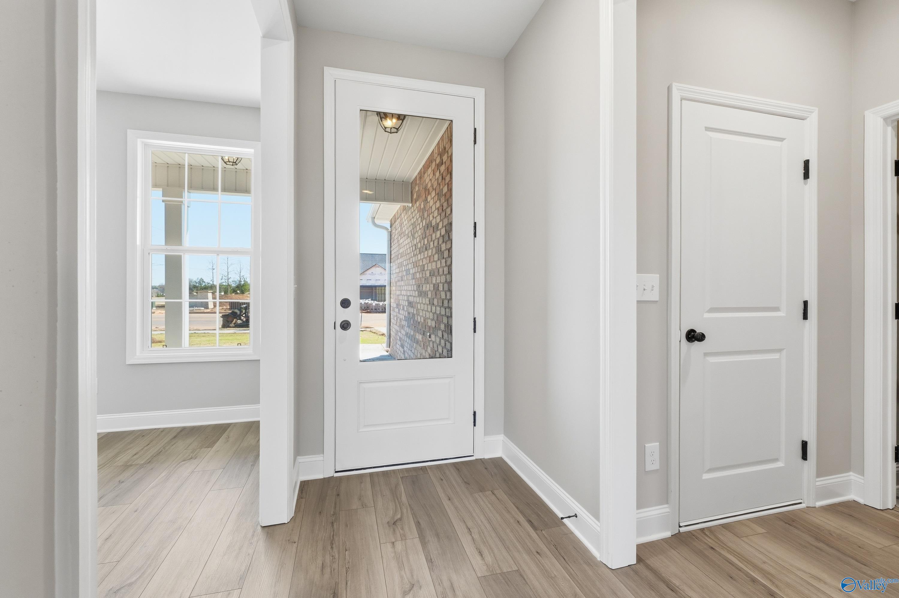 Bright hallway with frosted glass door to brick garage, white trim doors, and light wood floors in Davidson Homes The Rockford, Harvest, AL