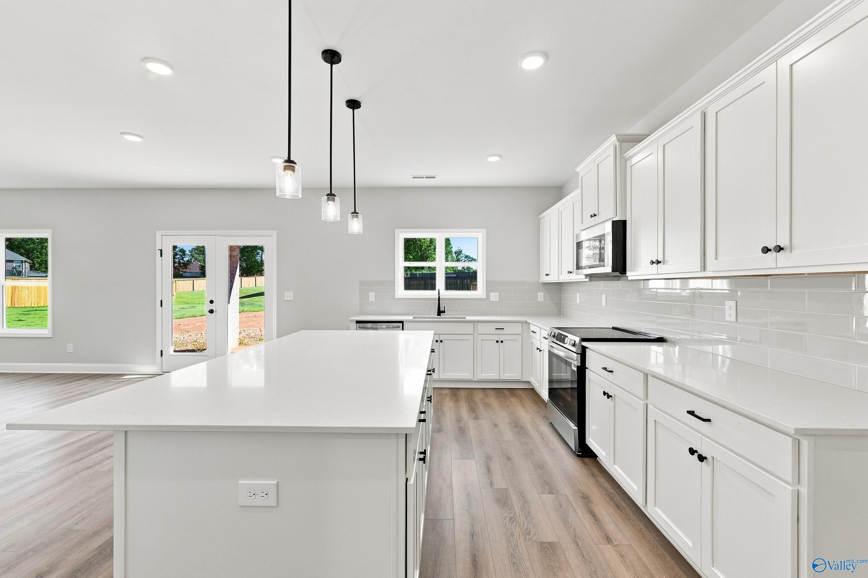 White kitchen with large island, pendant lights, stainless appliances, and luxury vinyl plank flooring in Davidson Homes Chelsea B, New Market, AL