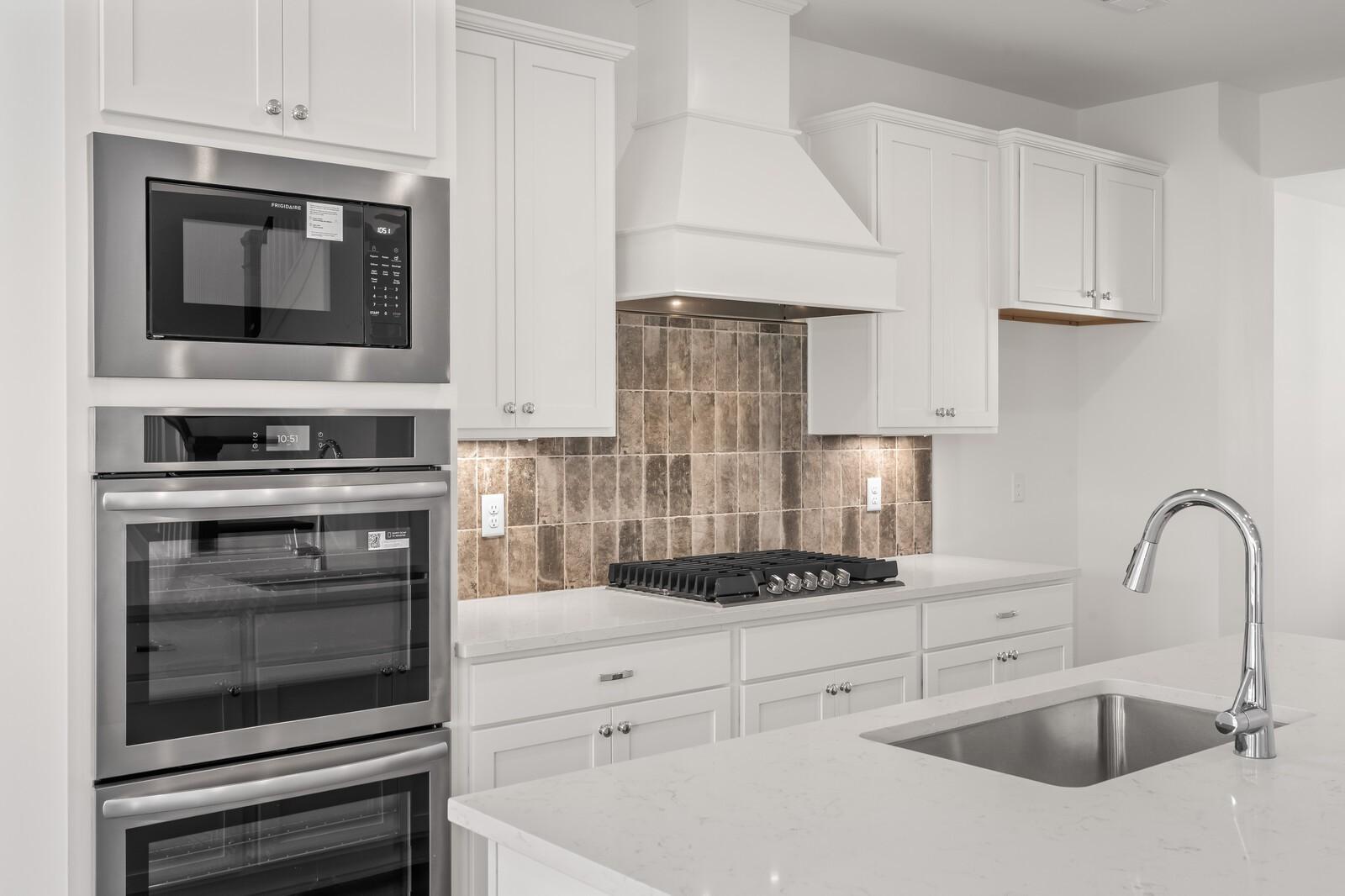Modern kitchen with white shaker cabinets, stainless double oven, gas cooktop, quartz island in Davidson Homes The Willow D, Mt. Juliet TN