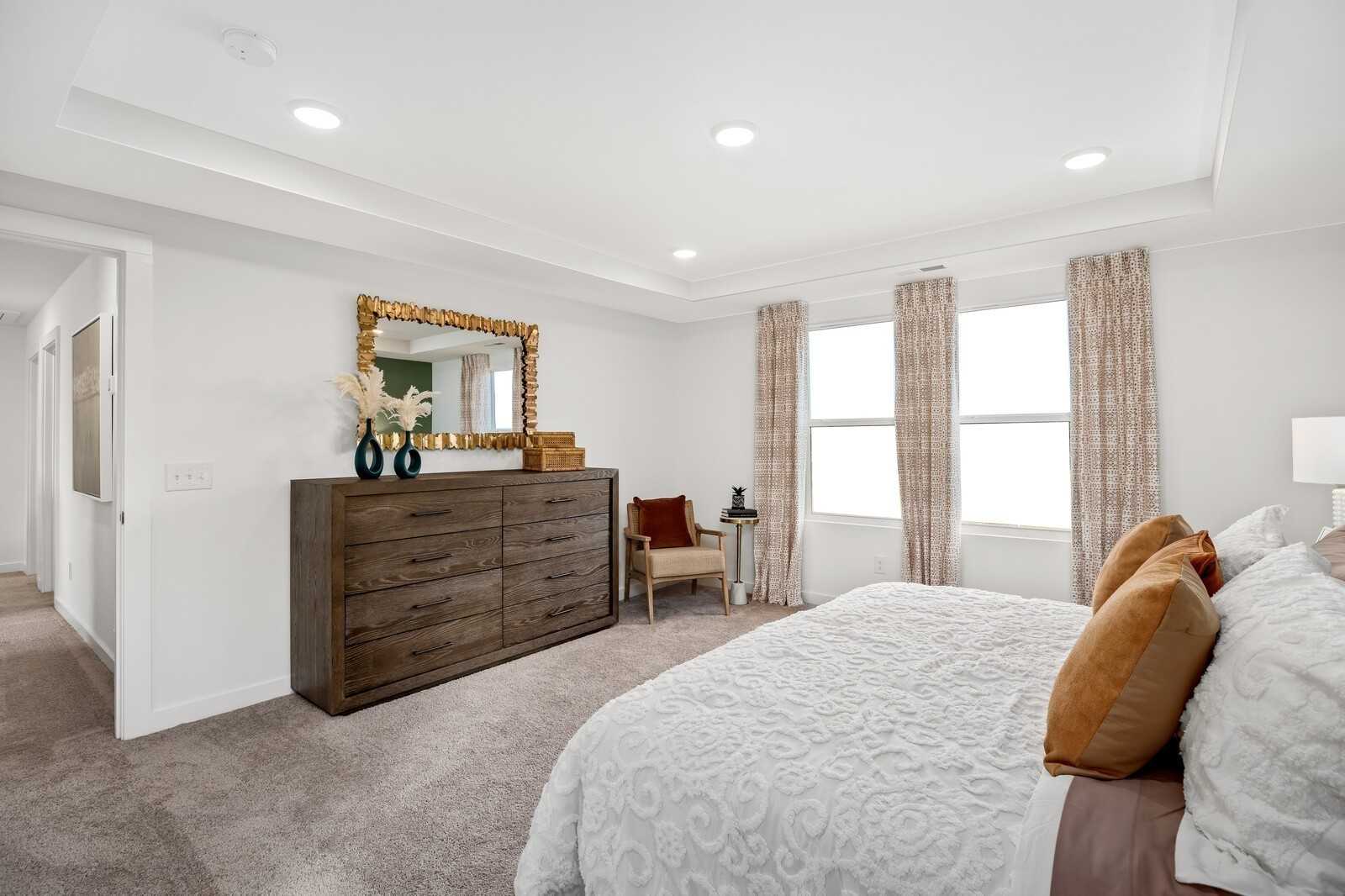 Elegant master bedroom with king bed, dark wood dresser, gold-framed mirror, and large windows in Davidson Homes The Gordon C, White House, TN