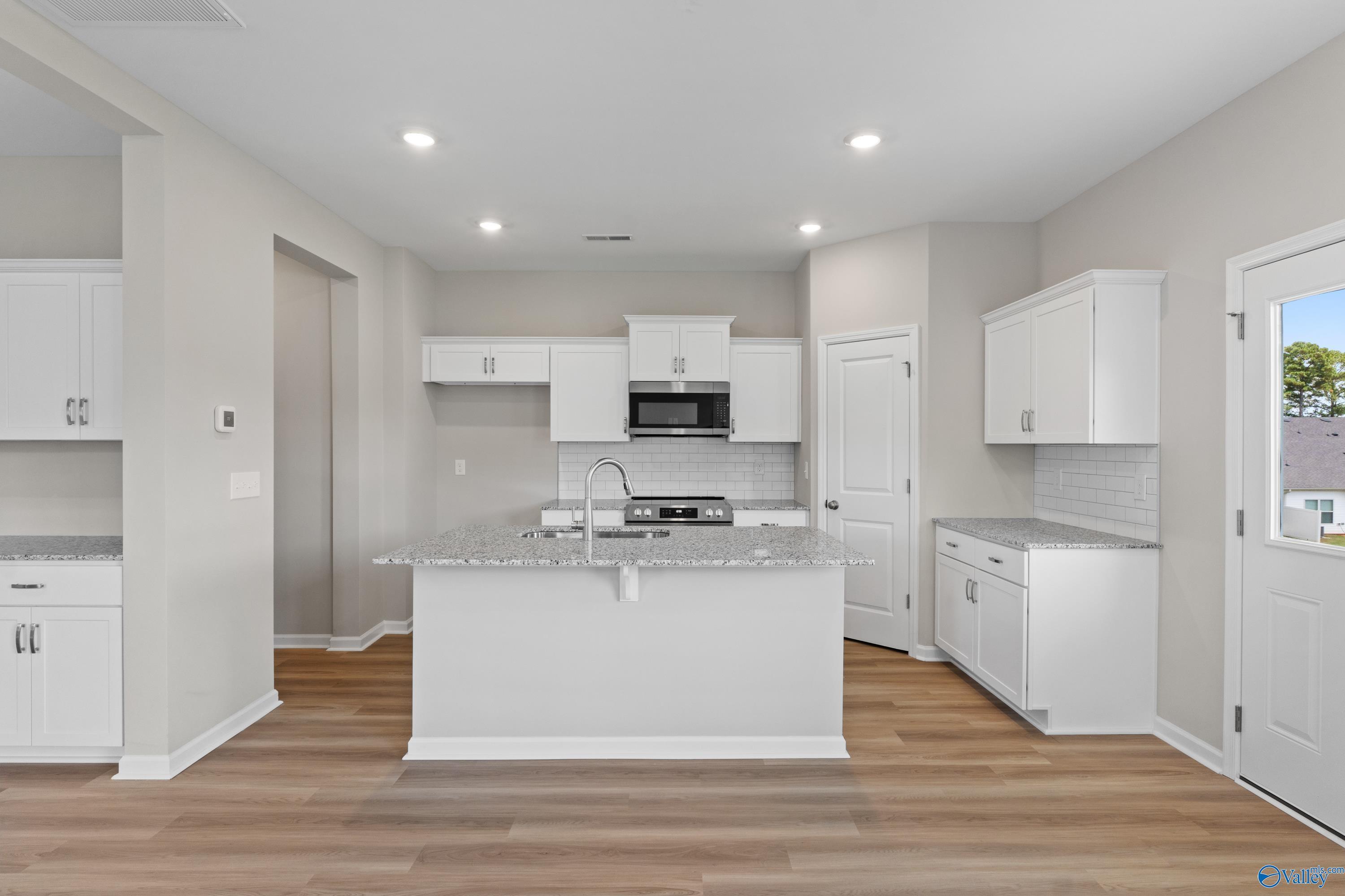 Modern white kitchen with granite island, stainless appliances, subway tile backsplash in Davidson Homes The Augusta, Madison AL