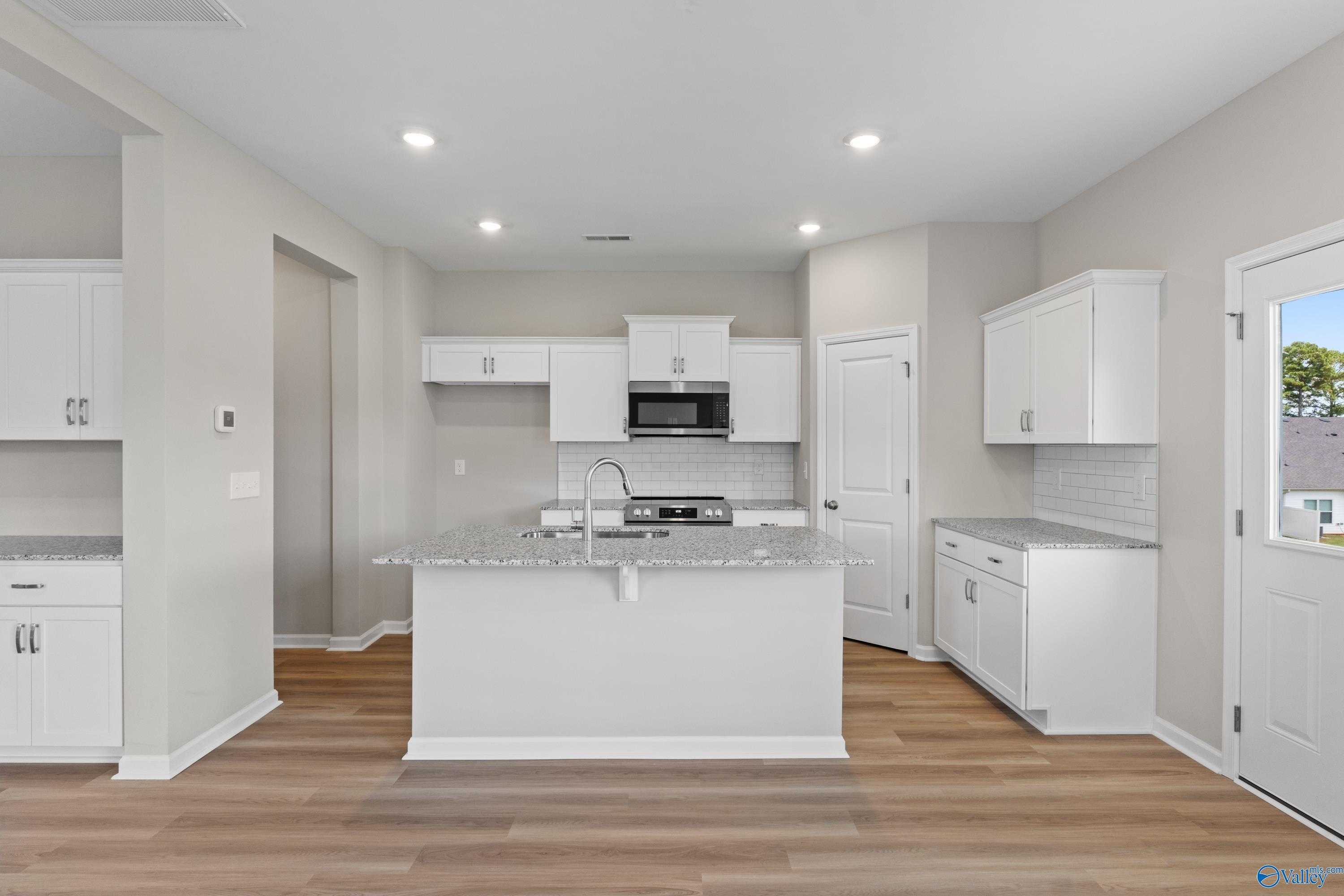 Modern white kitchen featuring granite island, stainless appliances, and subway tile in Evermore Homes The Augusta, Madison, Alabama
