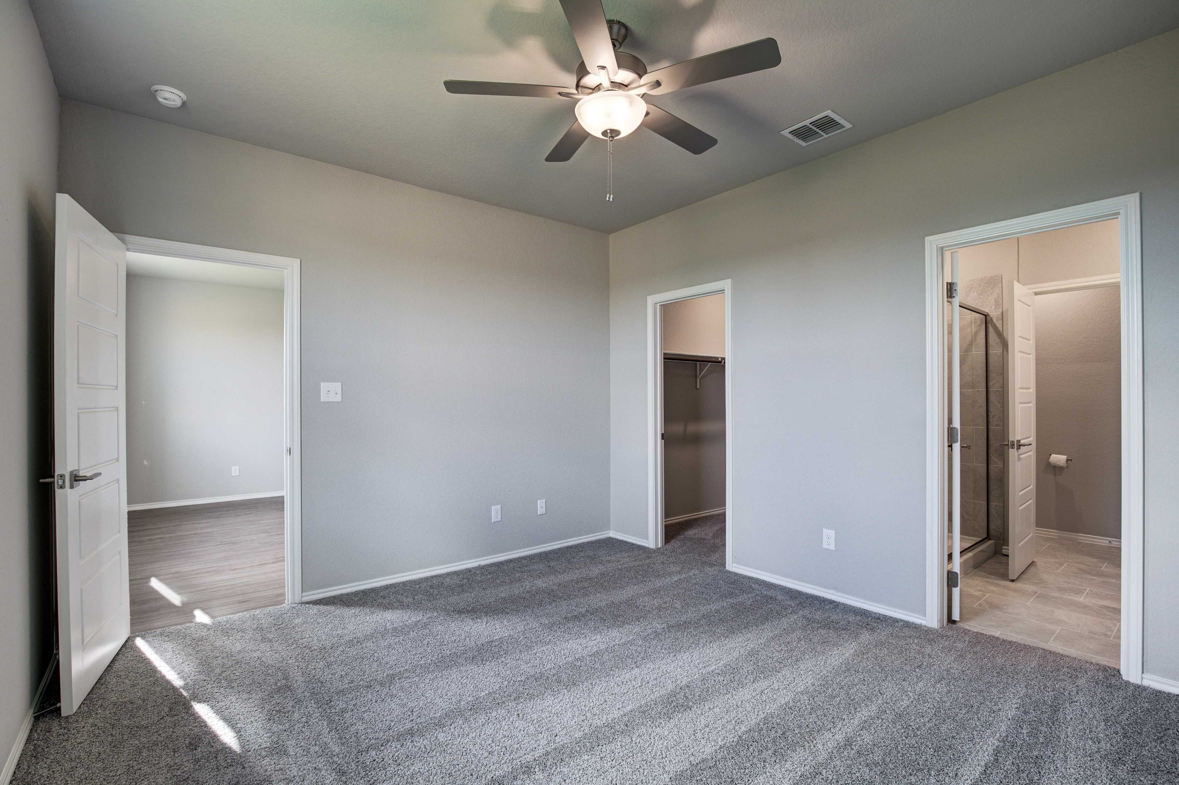 Spacious master bedroom in The Frio B with gray walls, carpet floor, ceiling fan, walk-in closet, and en-suite shower bath