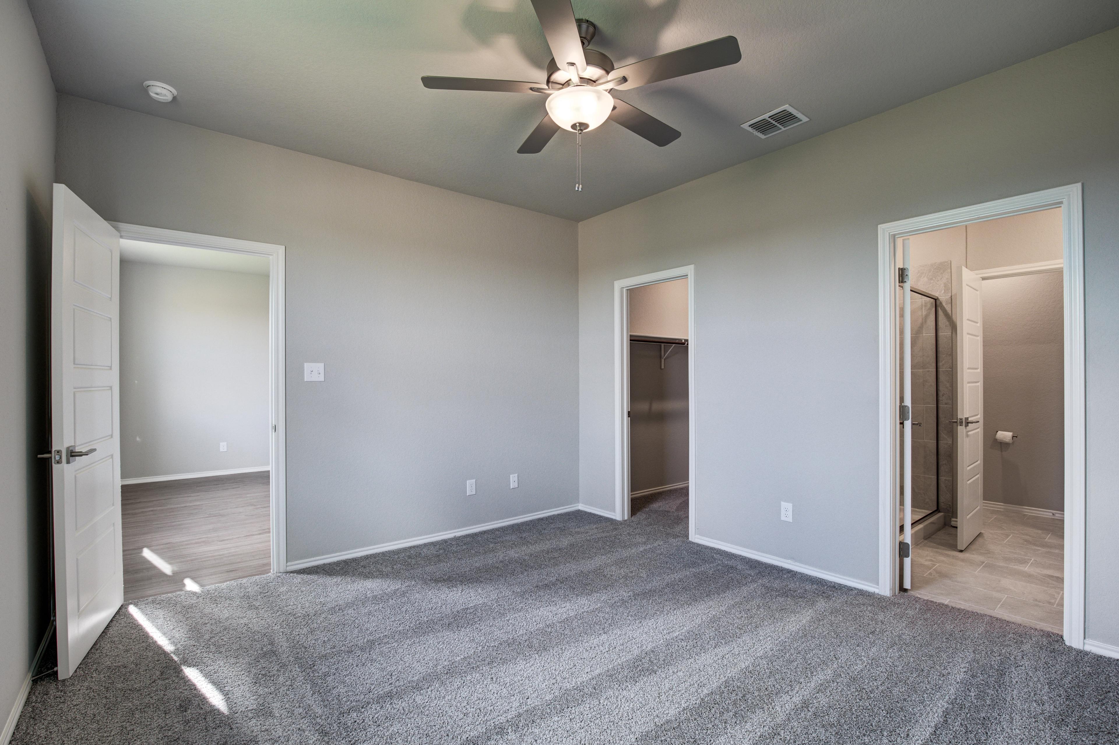 Spacious master bedroom in The Frio D with gray walls, carpeted floor, ceiling fan, walk-in closet, and en-suite bath