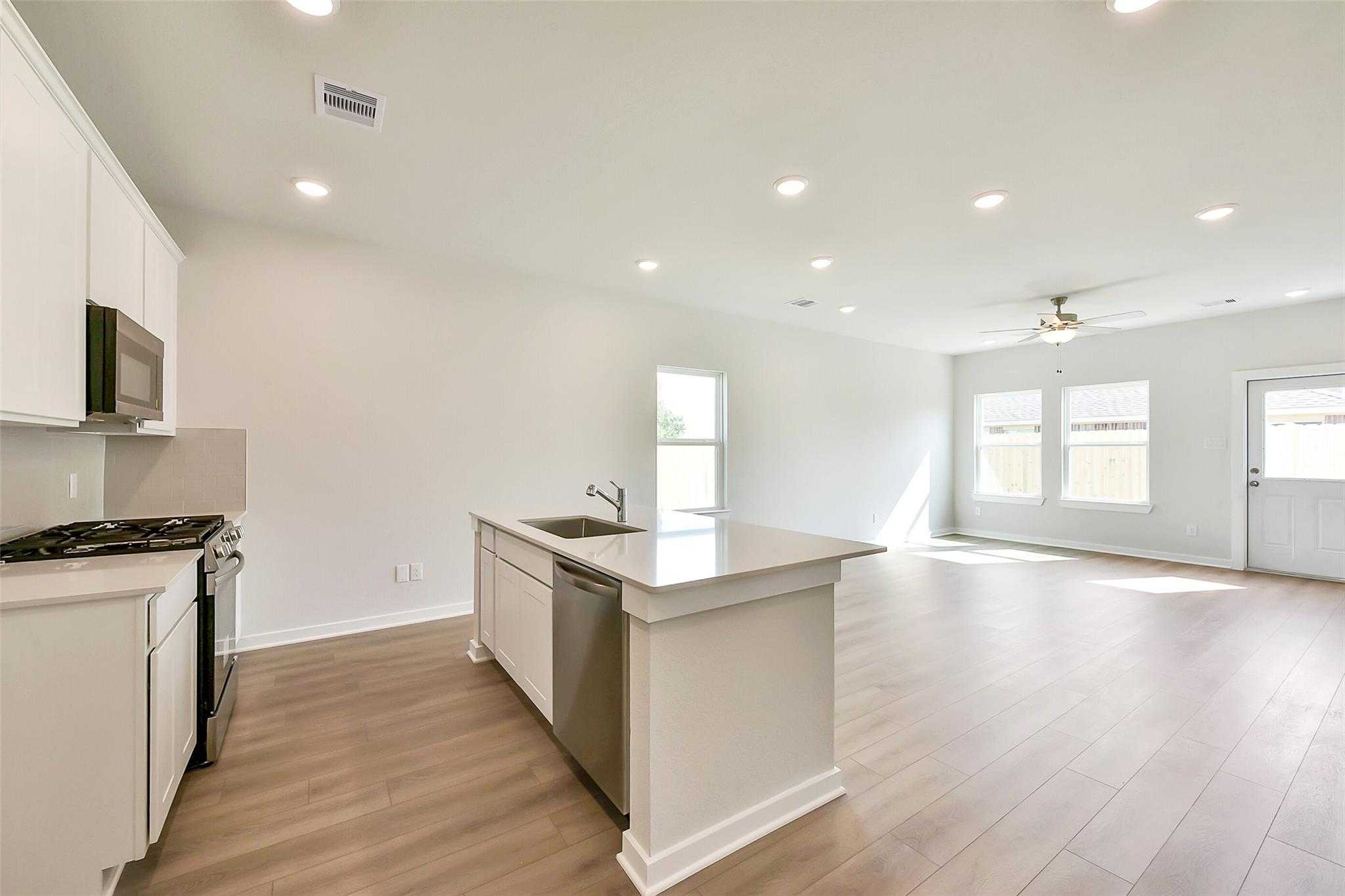 Bright open-concept kitchen with white cabinets, stainless appliances, center island, and adjacent living space in Davidson Homes Comal G, Dayton, Texas