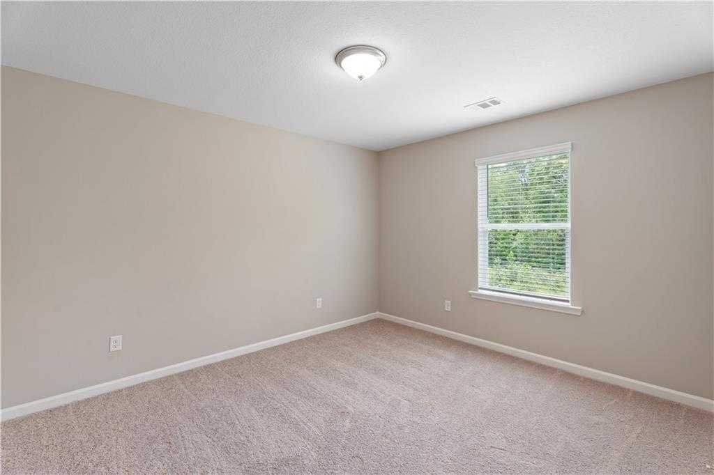 Bright empty bedroom featuring beige walls, plush carpet, and window with tree view in Davidson Homes The Bartlett, Phenix City, Alabama