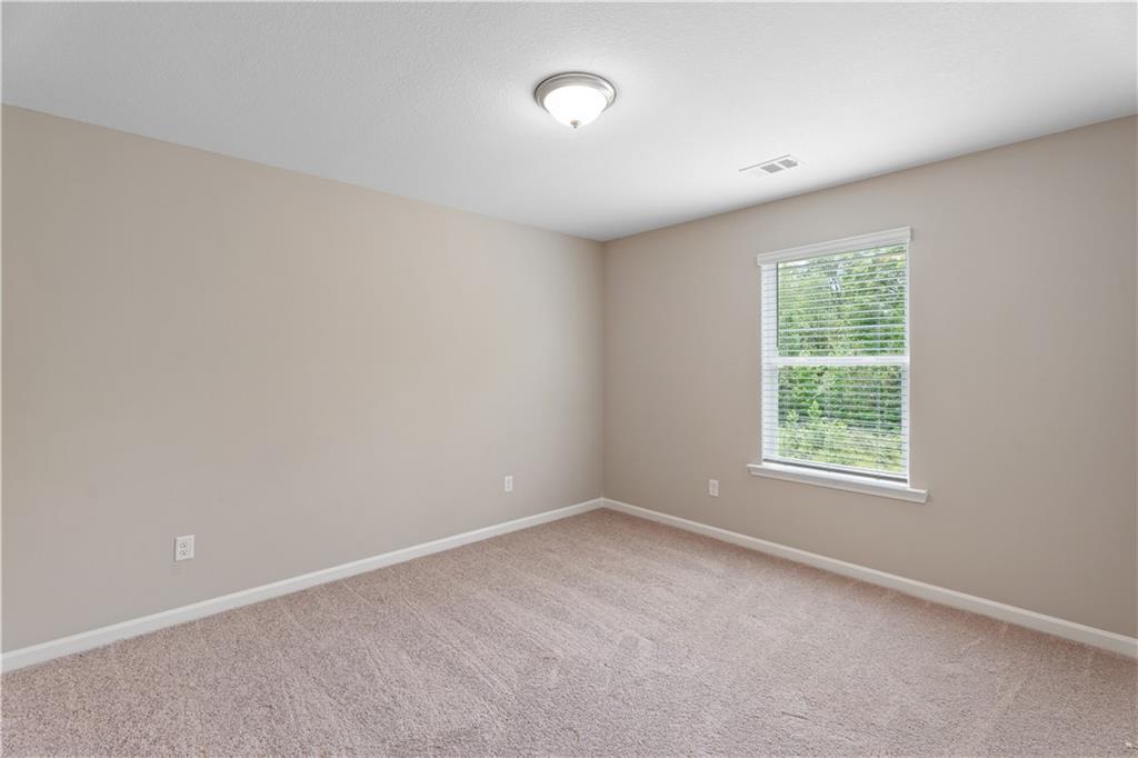 Bright empty bedroom featuring beige walls, plush carpet, and window with tree view in Davidson Homes The Bartlett, Phenix City, Alabama