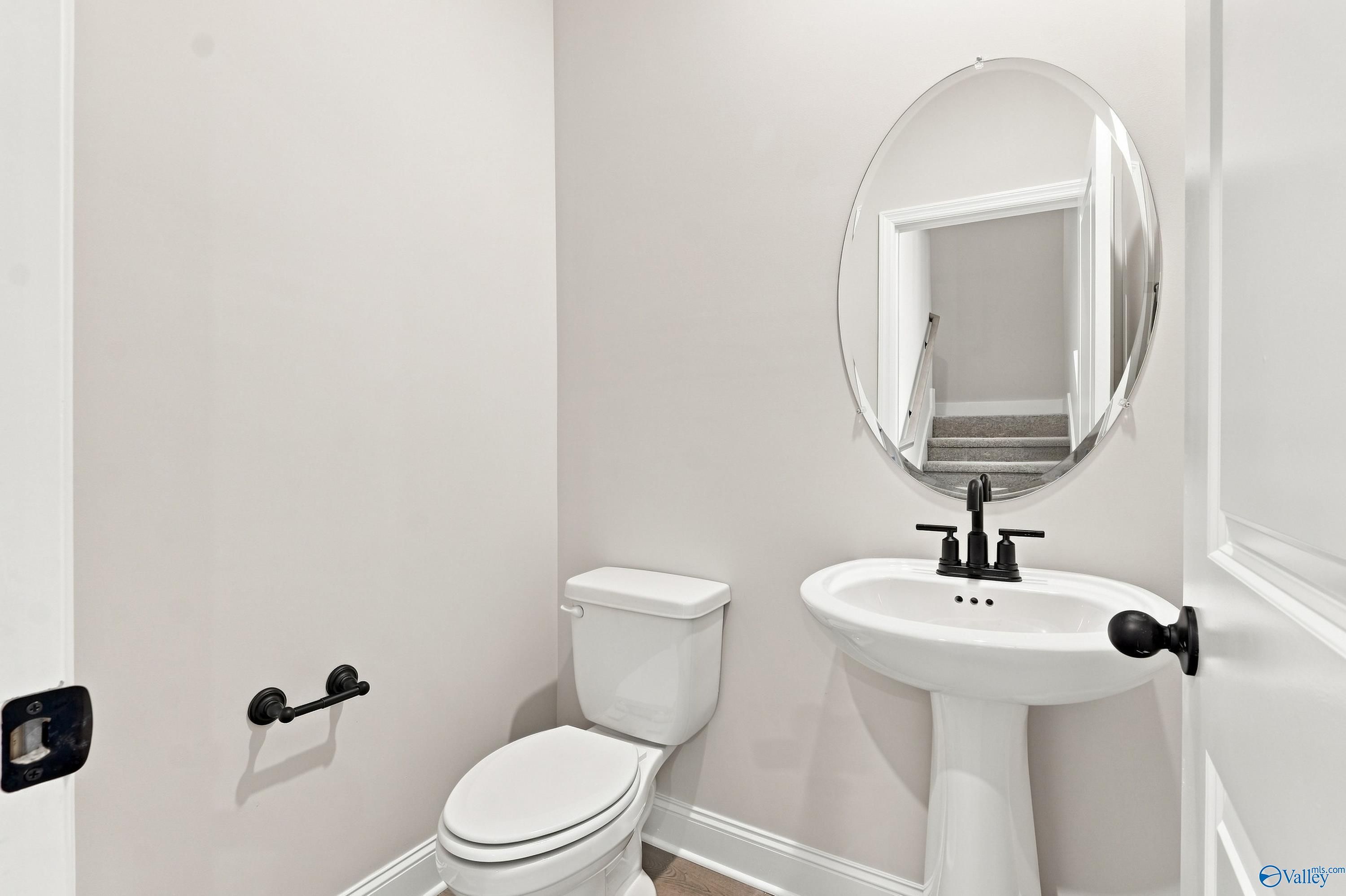 Half-bath with pedestal sink, oval mirror, and modern black fixtures in The Rockford B floor plan, Kendall Downs, Toney, AL.