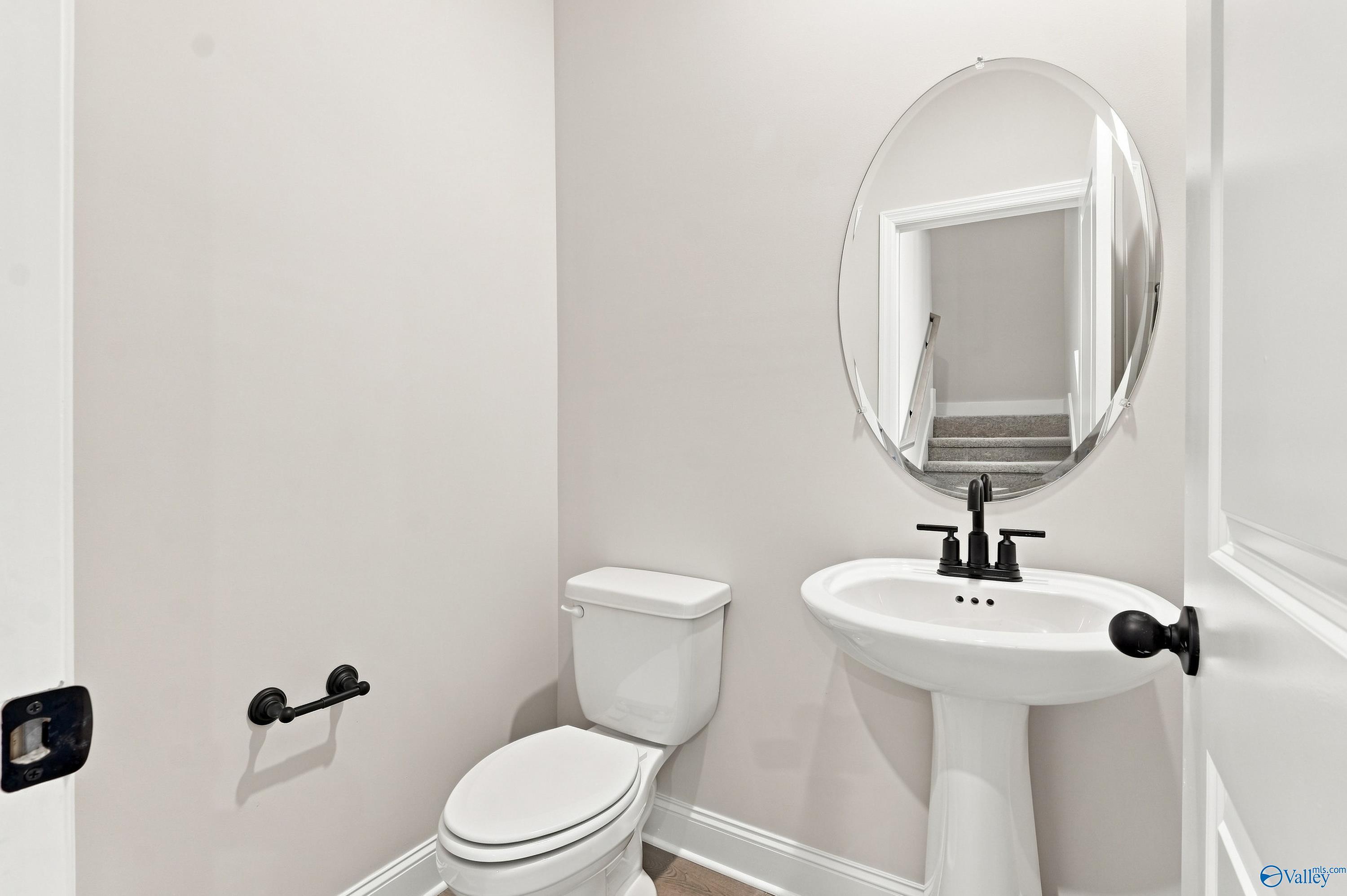 Half-bath with pedestal sink, oval mirror, and modern black fixtures in The Rockford B floor plan, Kendall Downs, Toney, AL.