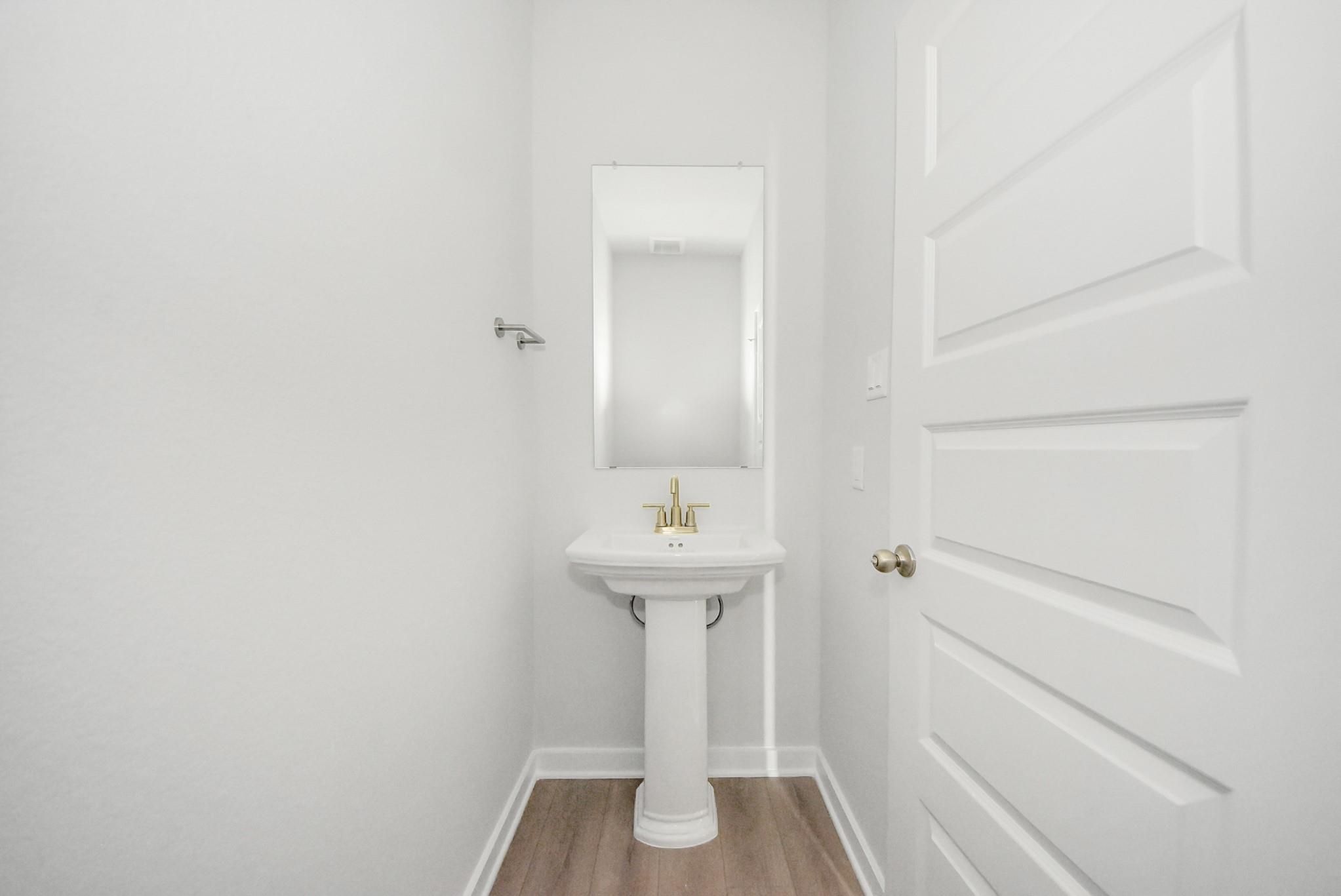 Modern powder room with pedestal sink, gold faucet, and mirror in Davidson Homes The Verano B floor plan, Sunterra, Katy.