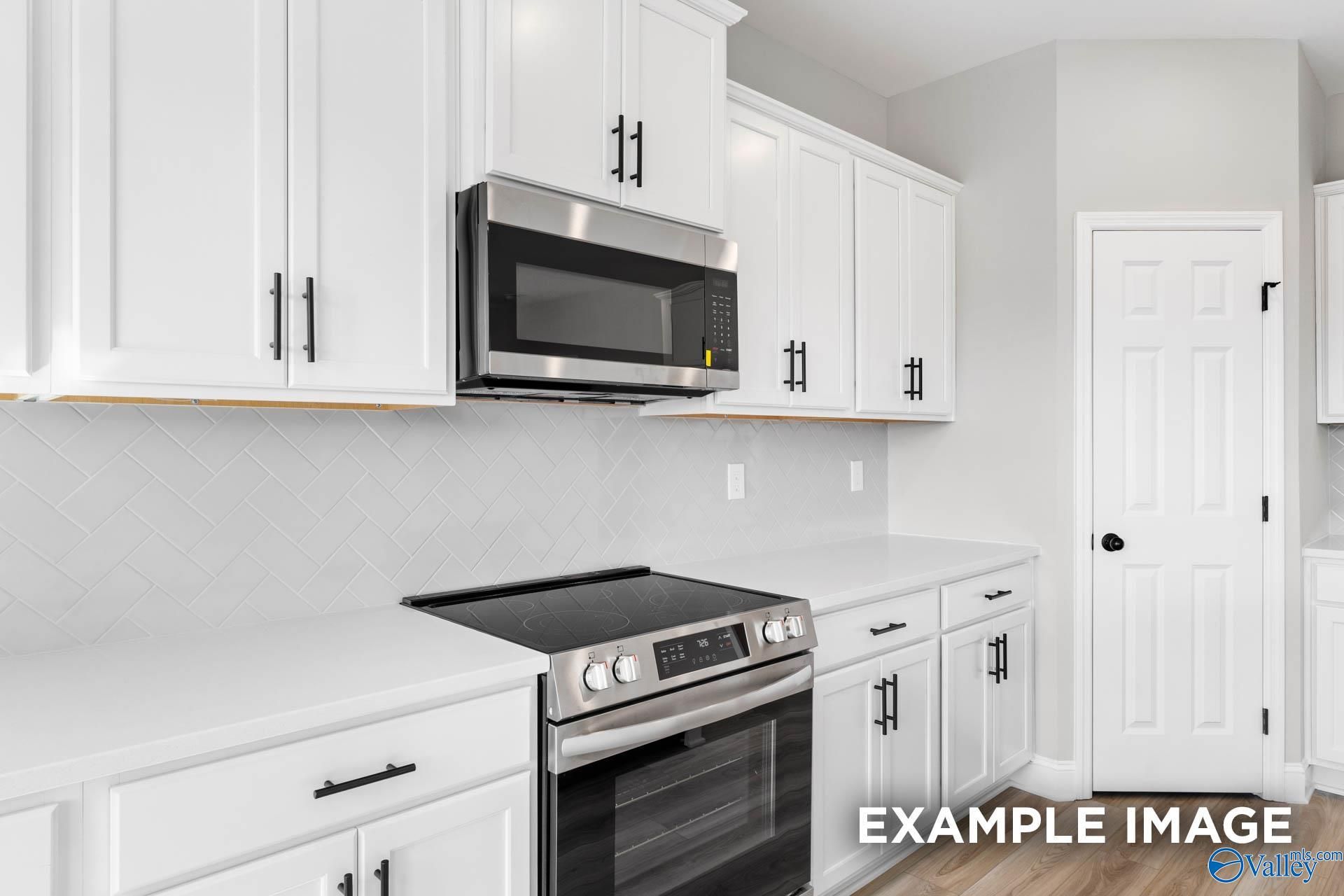 Modern kitchen with white cabinets, herringbone backsplash, and stainless appliances in The Madison D at Evergreen Mill.