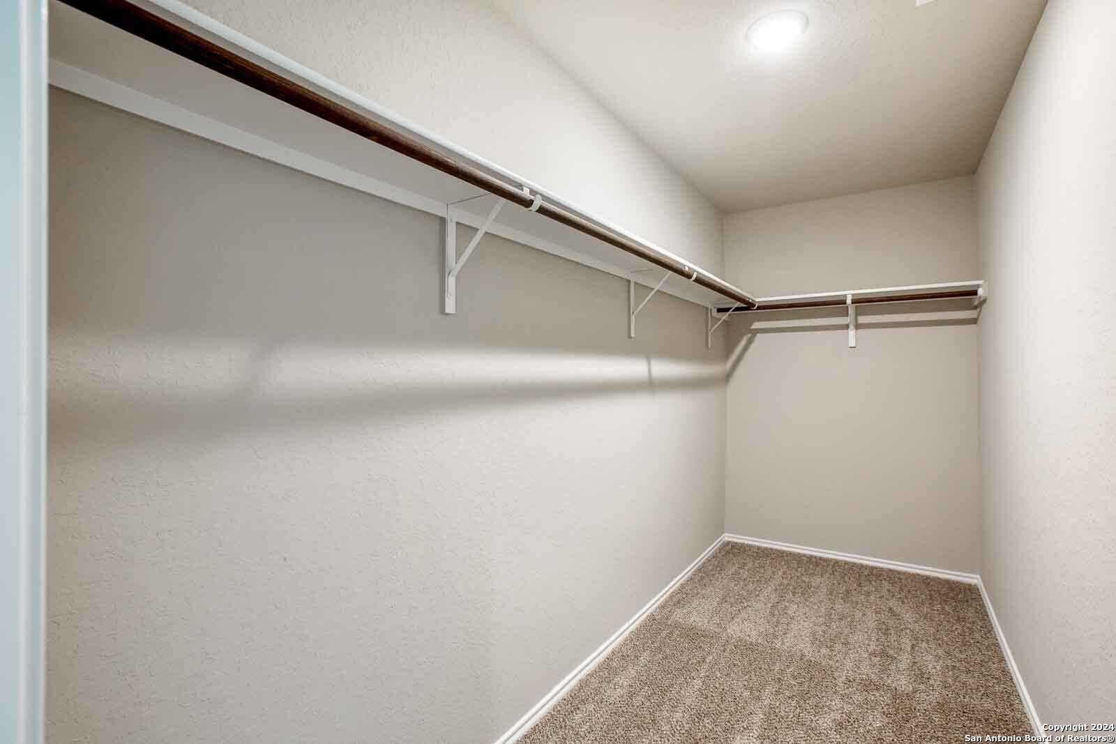 Spacious walk-in closet with double wooden rods, beige walls, and carpeted floor in Davidson Homes The Murray H, Seguin, Texas