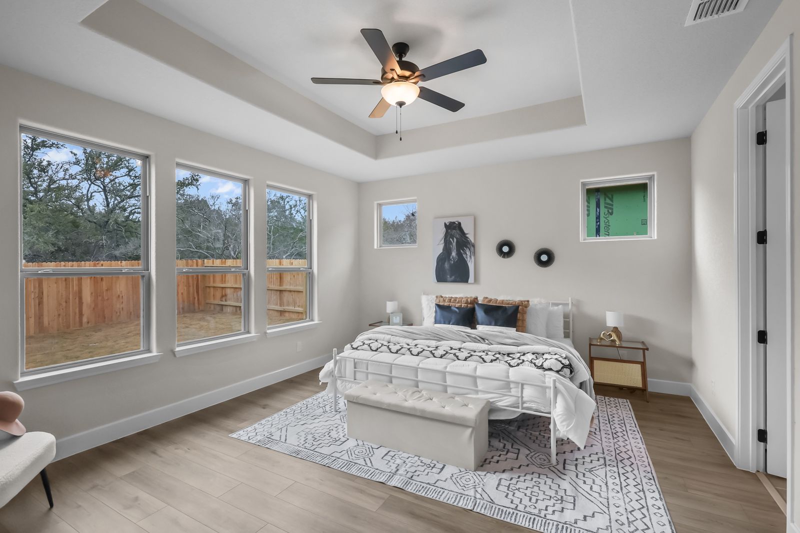 Spacious master suite on main floor in The Belmont J featuring tray ceilings, large windows, and modern bedroom decor.