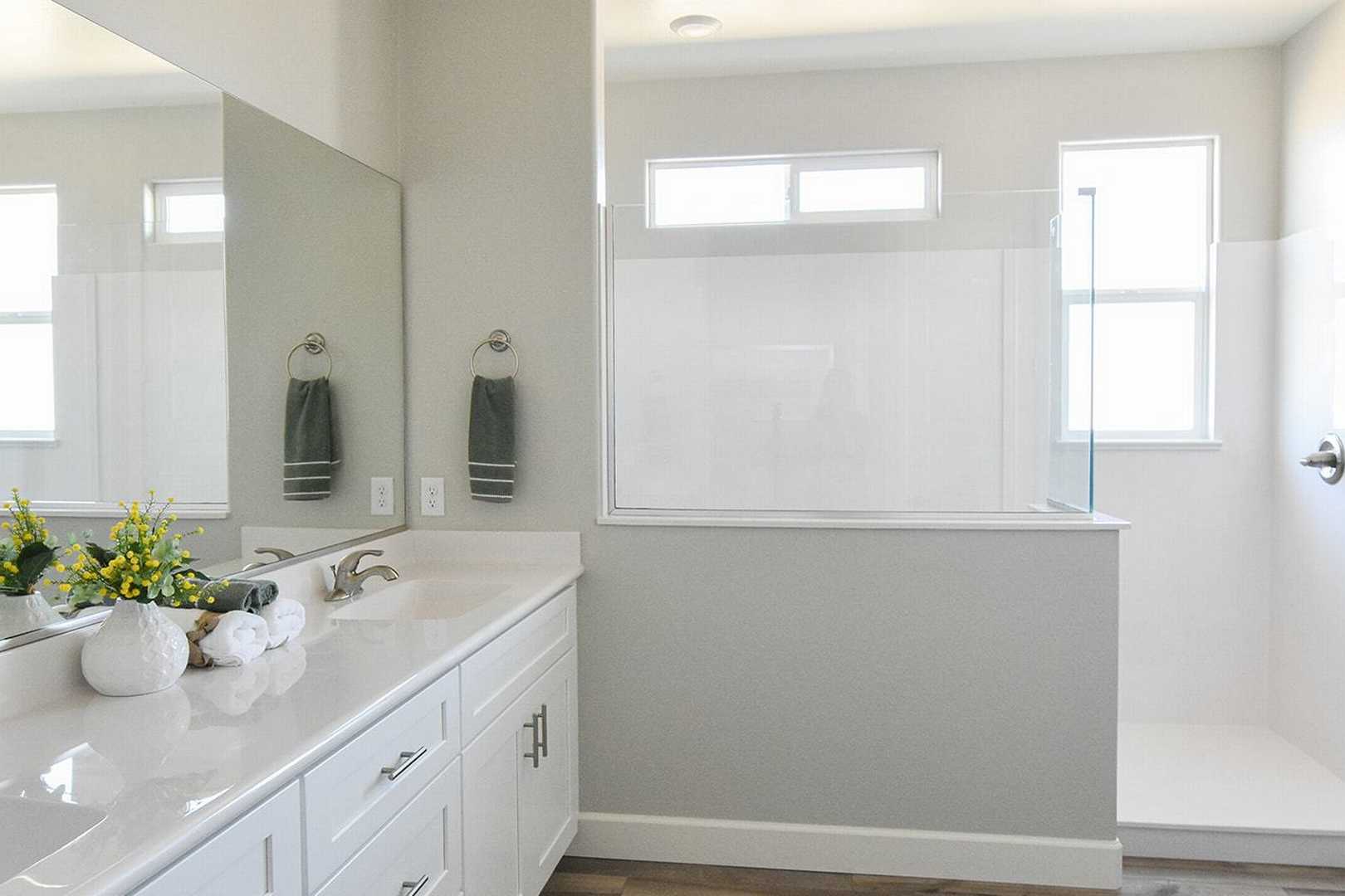 Spacious master bathroom in The Summit B featuring double vanity, large mirror, and frameless walk-in shower