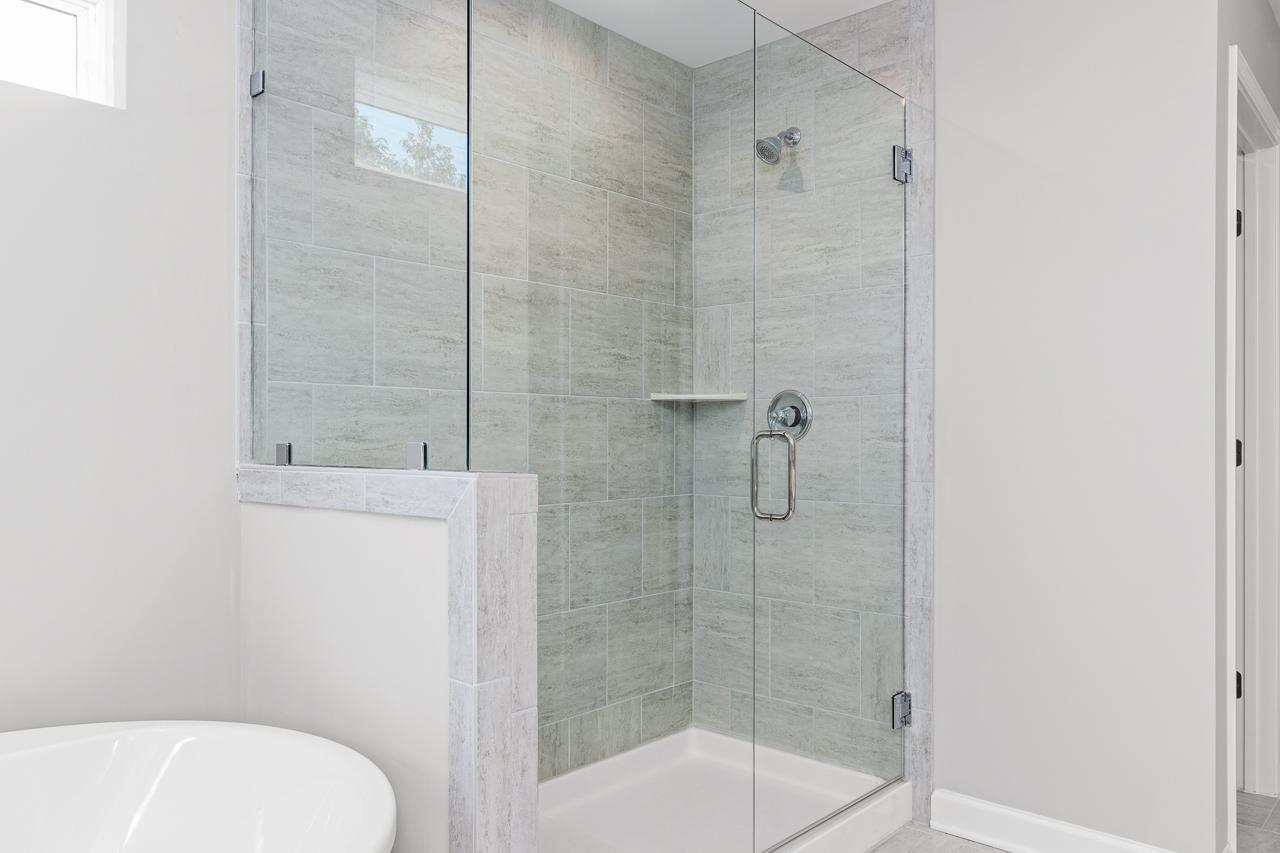 Modern glass-enclosed walk-in shower with grey tiled walls in the master bathroom of The Hemlock in Belmont, NC.