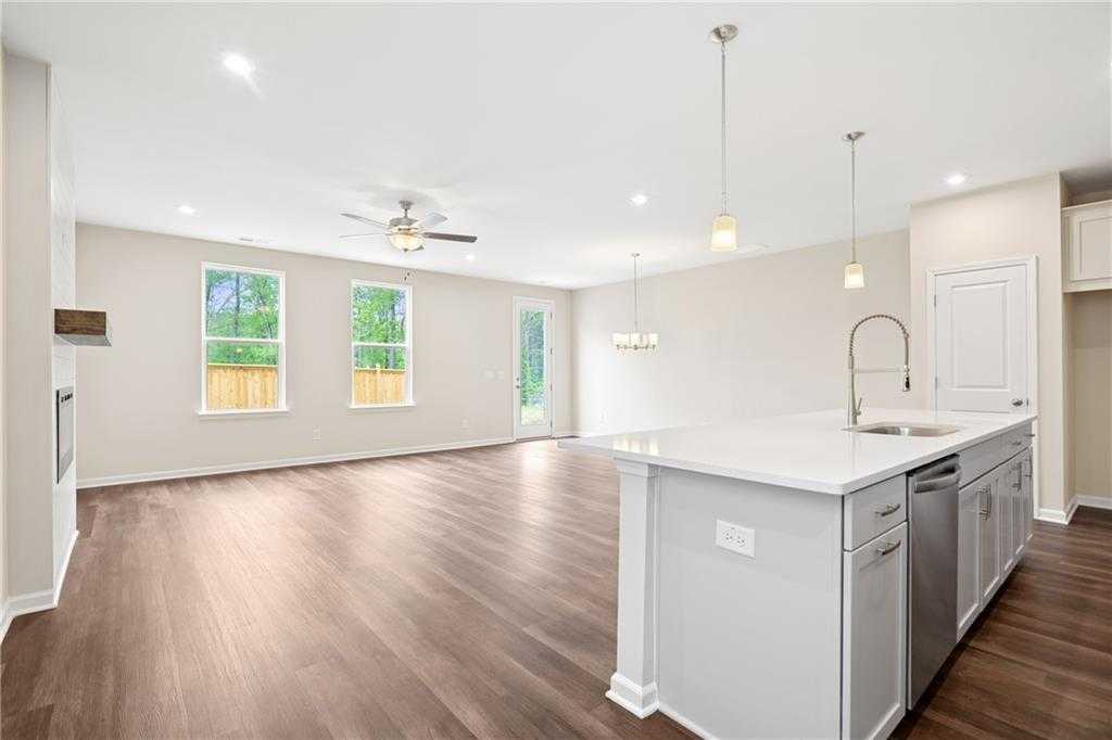 Bright open-concept kitchen and living room with white island, hardwood floors, ceiling fan, and large windows in Davidson Homes Cary B, Kennesaw GA
