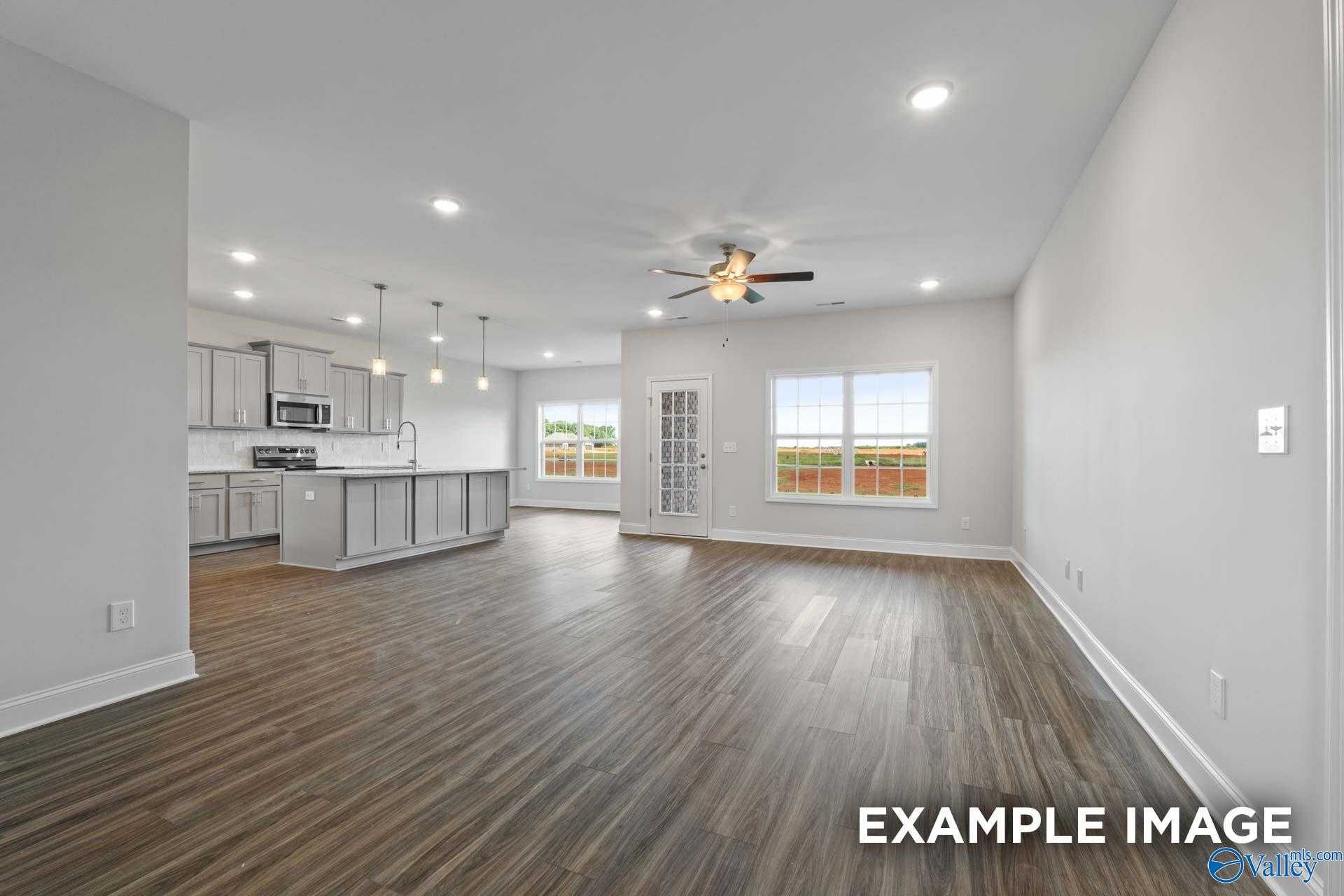 Open-concept kitchen-living area with gray cabinets, island, ceiling fan, hardwood floors, and large windows in Davidson Homes The Montgomery, Athens AL