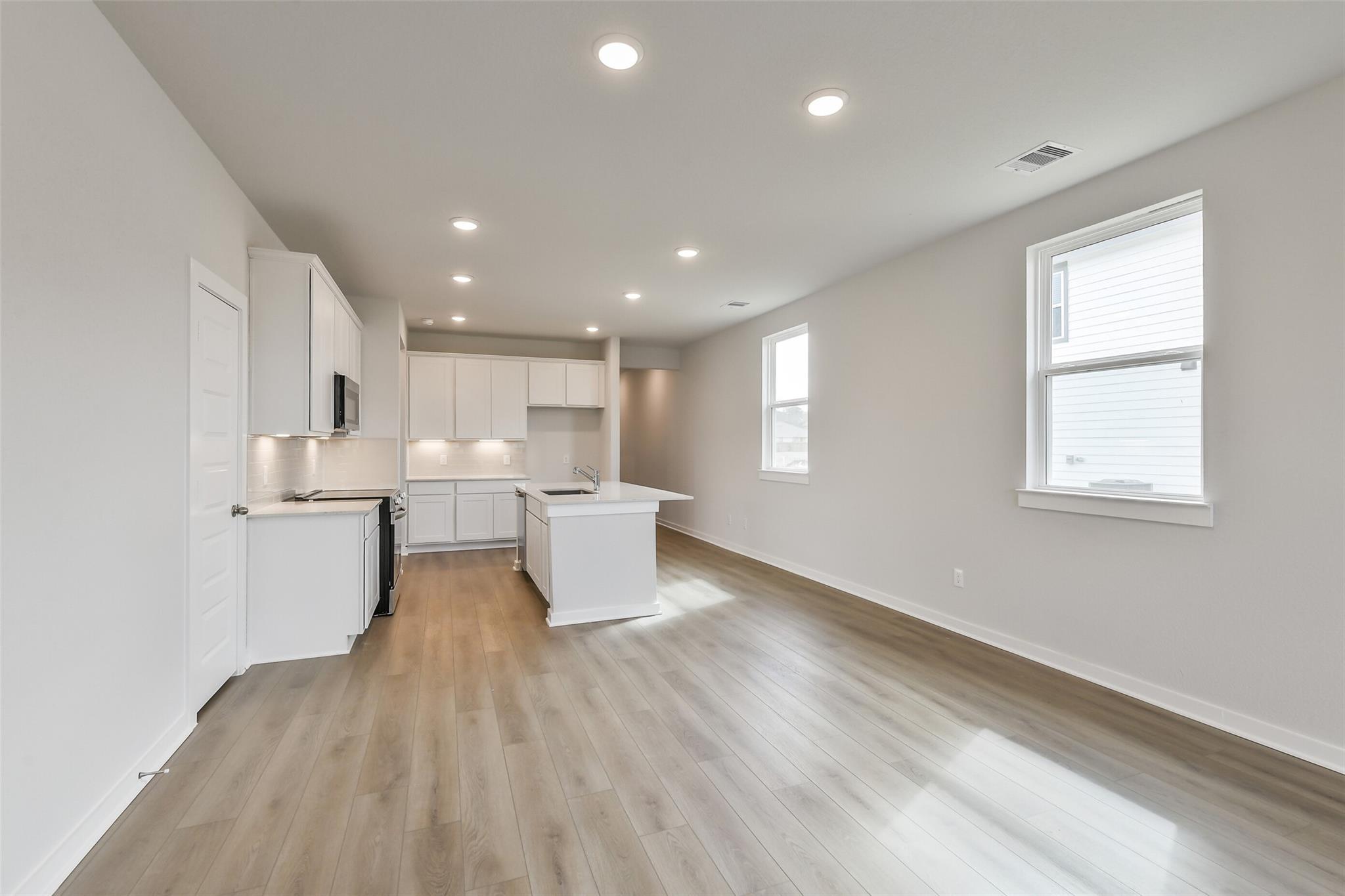 Modern open-concept kitchen with white cabinets, stainless appliances, and light wood floors in The Frio G home, Cleveland Texas