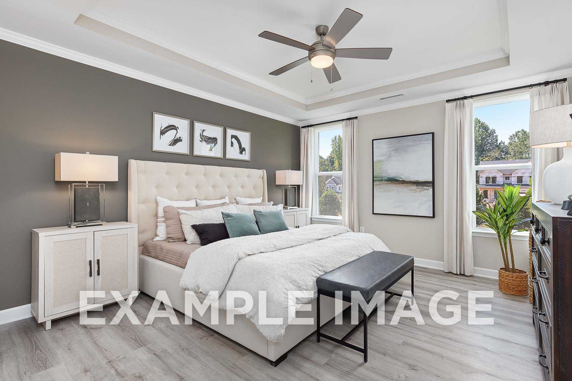 Spacious master bedroom in The Ash E featuring tufted king bed, ceiling fan, modern art, and large window with plant