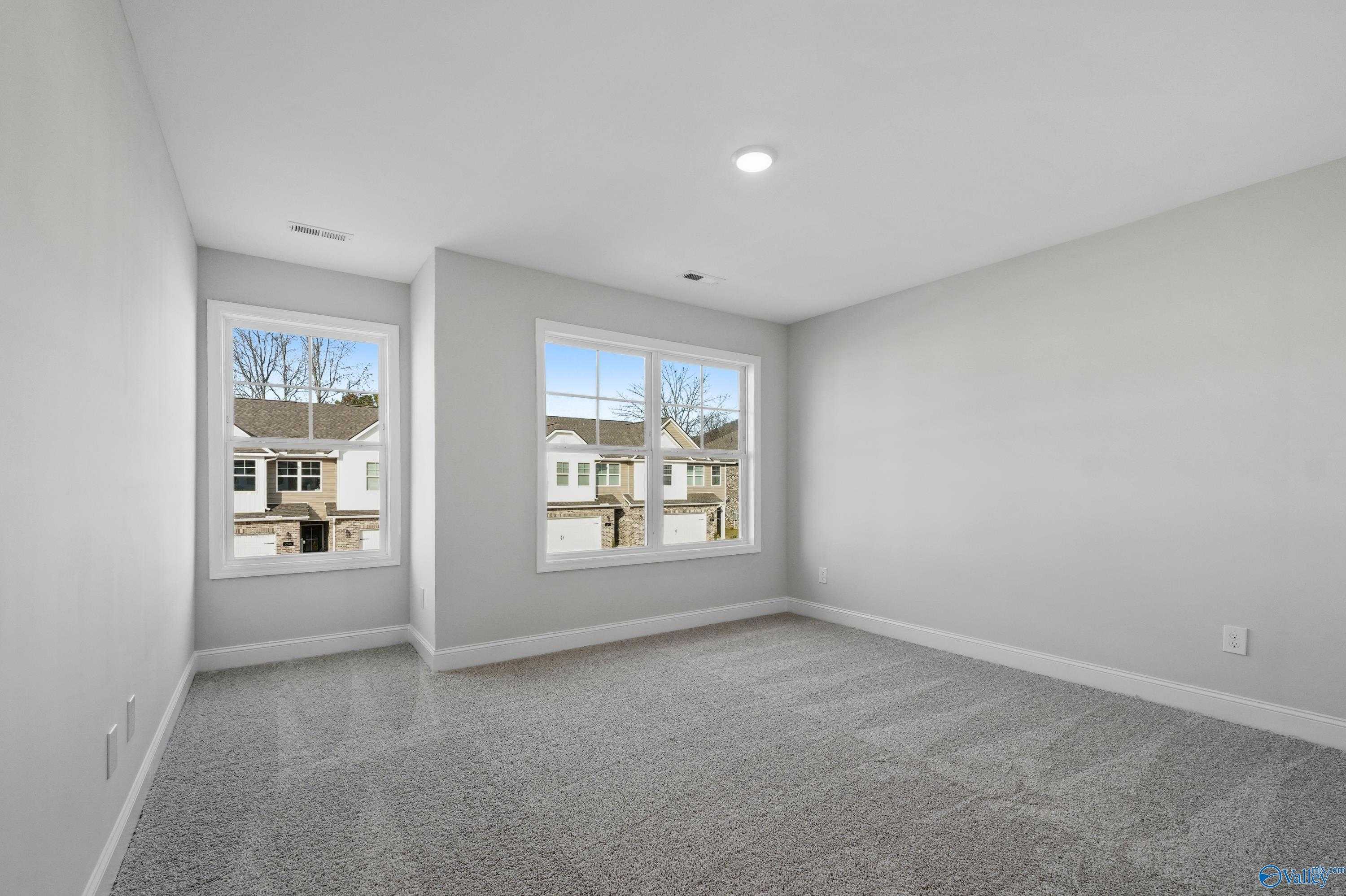 Spacious secondary bedroom with gray carpet, light walls, and large windows overlooking neighborhood in The Camden, Huntsville, AL
