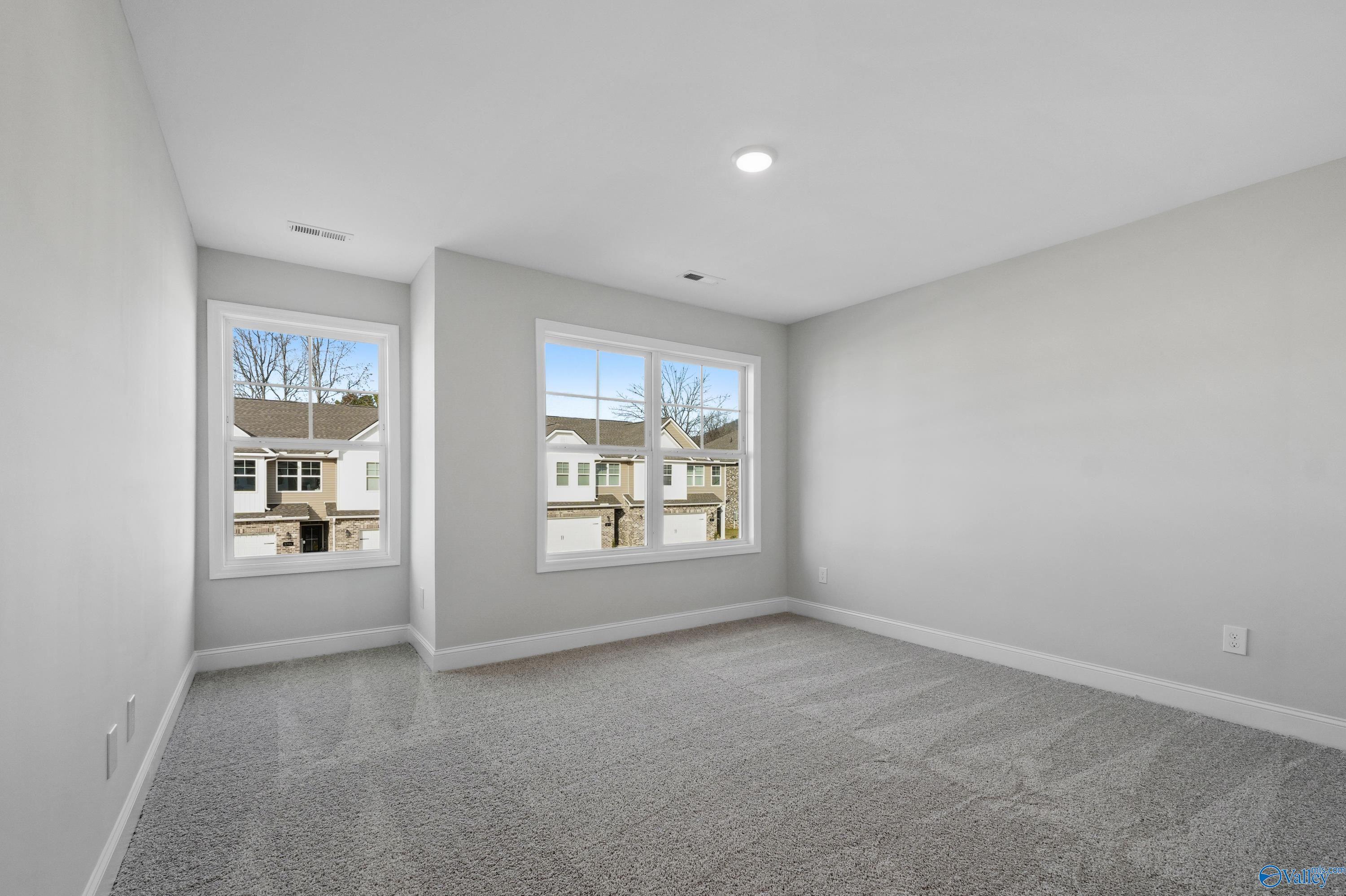 Bright secondary bedroom with light gray walls, plush carpet, large windows overlooking suburban homes in Davidson Homes The Camden, Huntsville AL