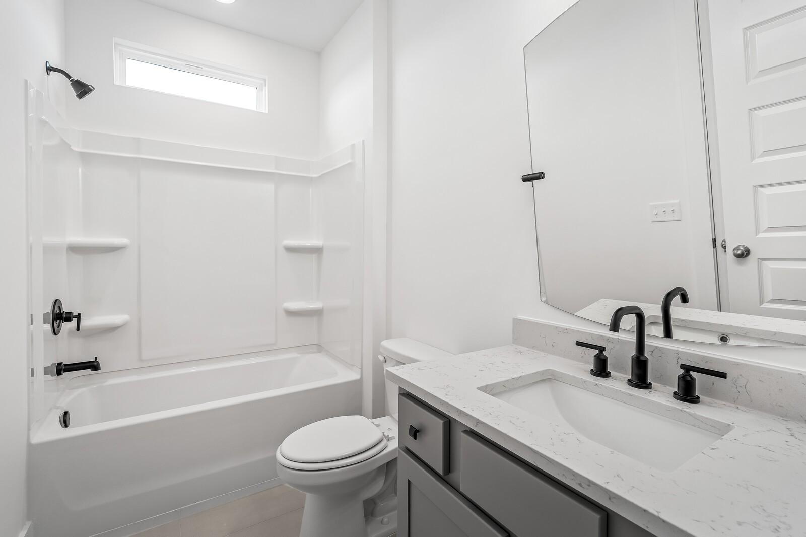 Modern bathroom with white tiled shower-tub combo, quartz vanity, gray cabinets, and frameless mirror in The Alston A, Murfreesboro, TN
