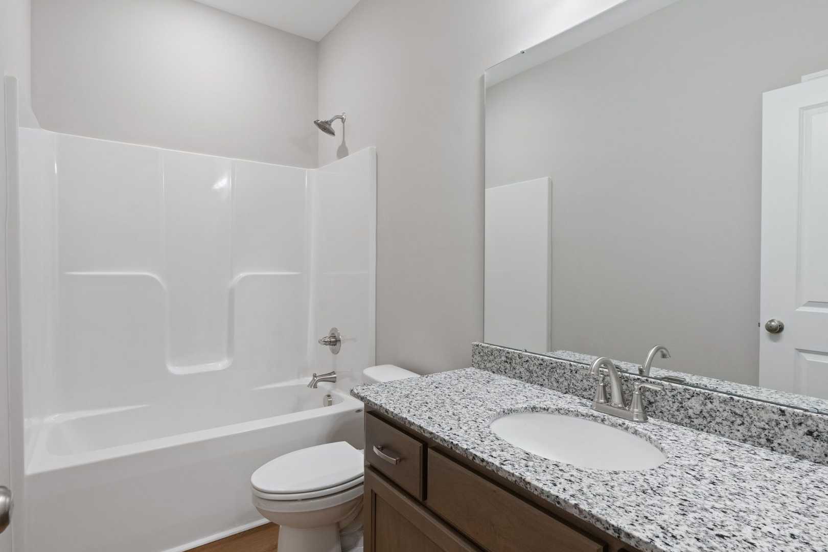 Spacious bathroom in The Luna featuring white tub-shower combo, granite vanity, modern sink, and neutral walls