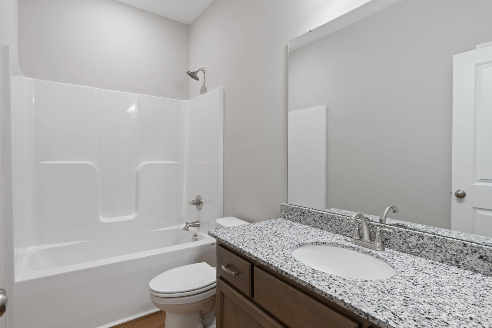 Spacious bathroom in The Luna featuring white tub-shower combo, granite vanity, modern sink, and neutral walls