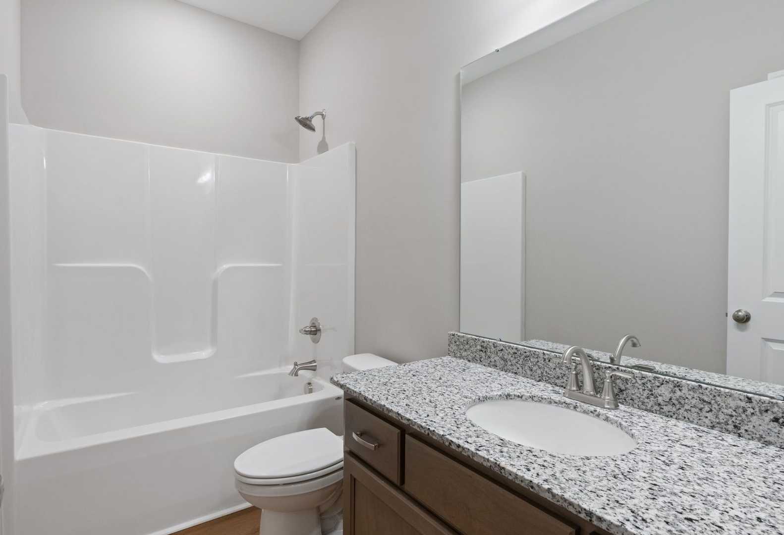 Modern guest bathroom in The Luna A showcasing white tub, walk-in shower, granite vanity, and wood floors