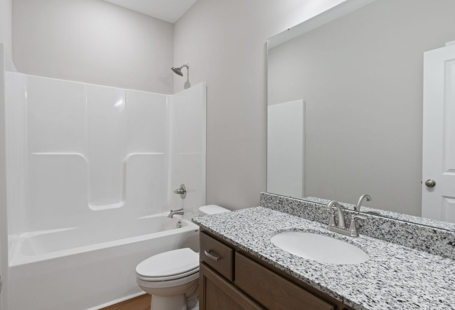 Modern guest bathroom in The Luna A showcasing white tub, walk-in shower, granite vanity, and wood floors