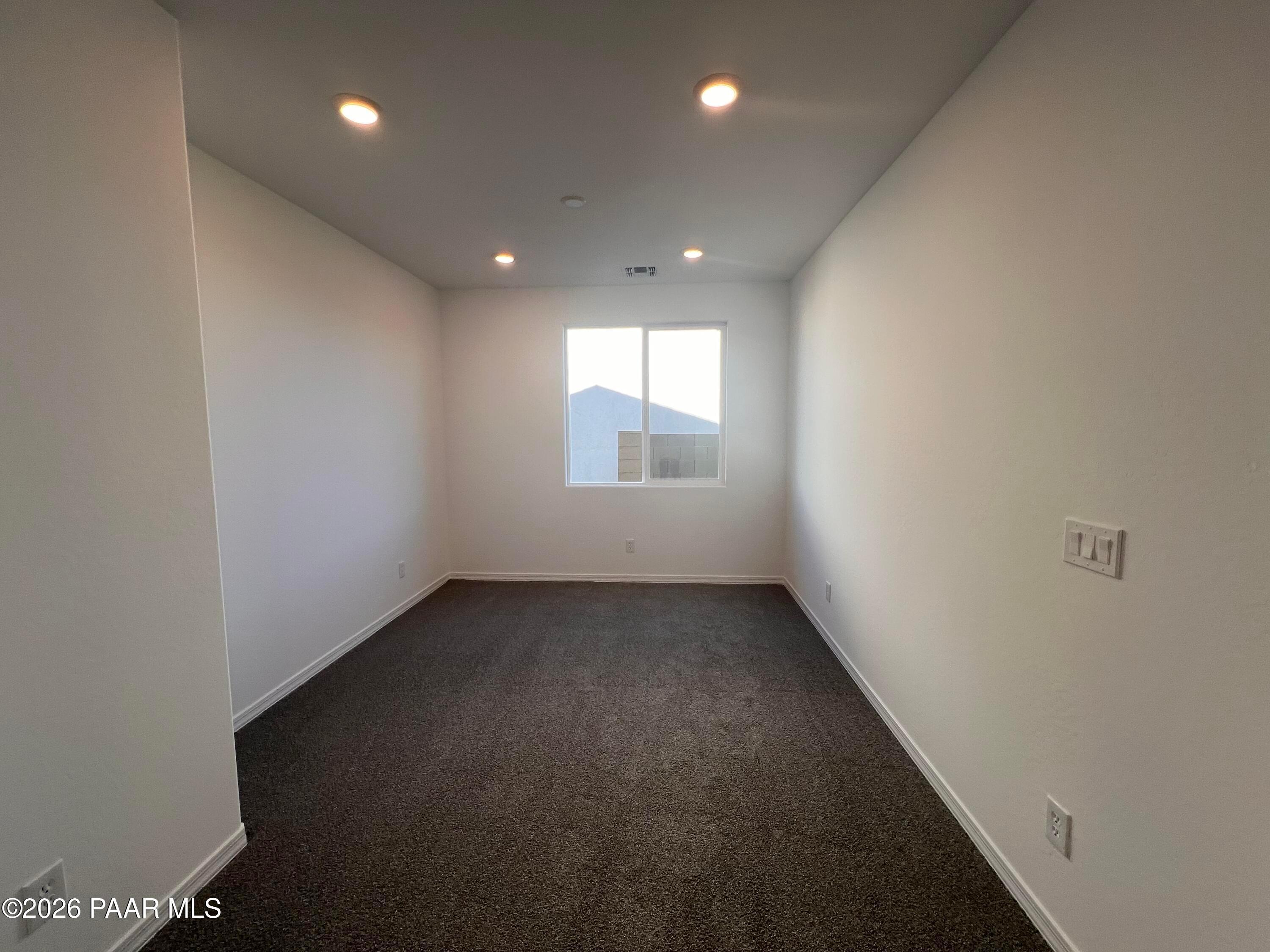 Spacious empty bedroom with white walls, brown carpet, large window and recessed lights in Davidson Homes Sunrise II A, Prescott AZ