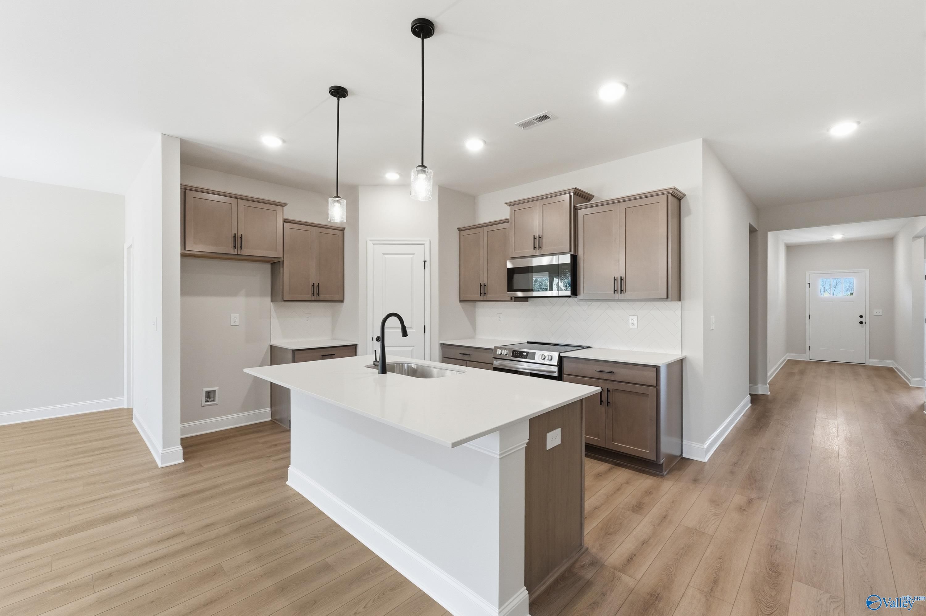 Modern kitchen featuring taupe shaker cabinets, white quartz island with sink, stainless appliances in Davidson Homes The Daphne C, New Market, Alabama