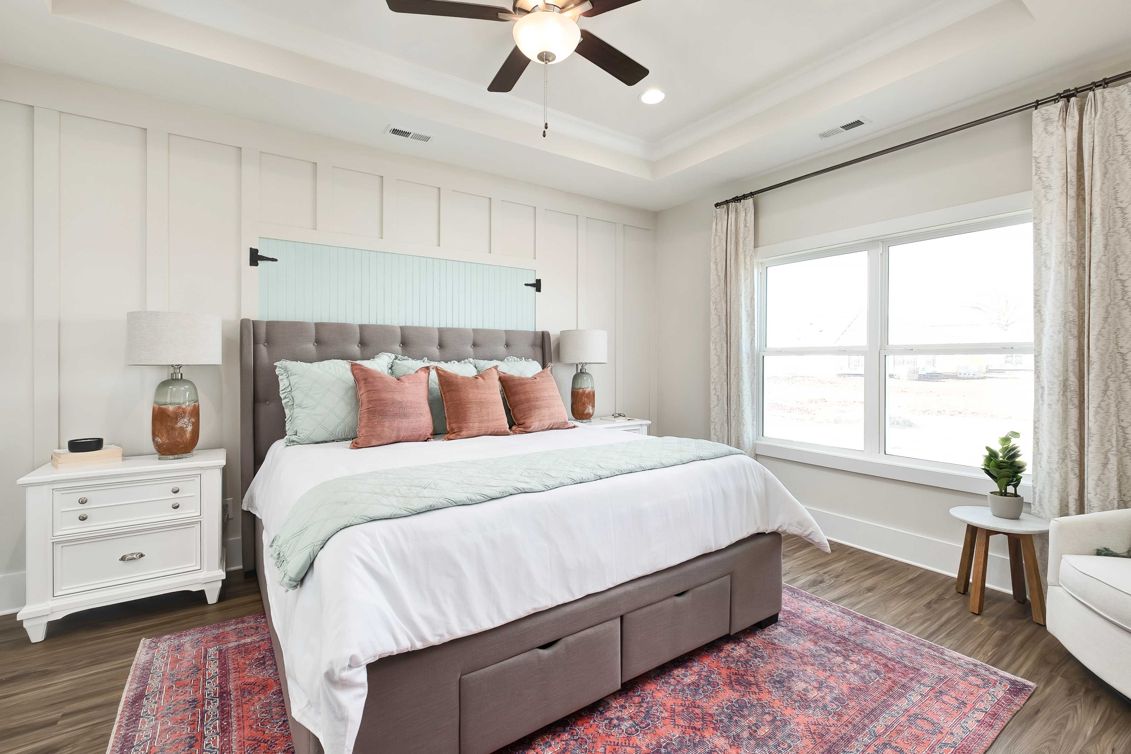 Cozy master bedroom at Mallard Landing in Athens Alabama featuring shiplap walls, tufted gray headboard bed, ceiling fan, and hardwood floors