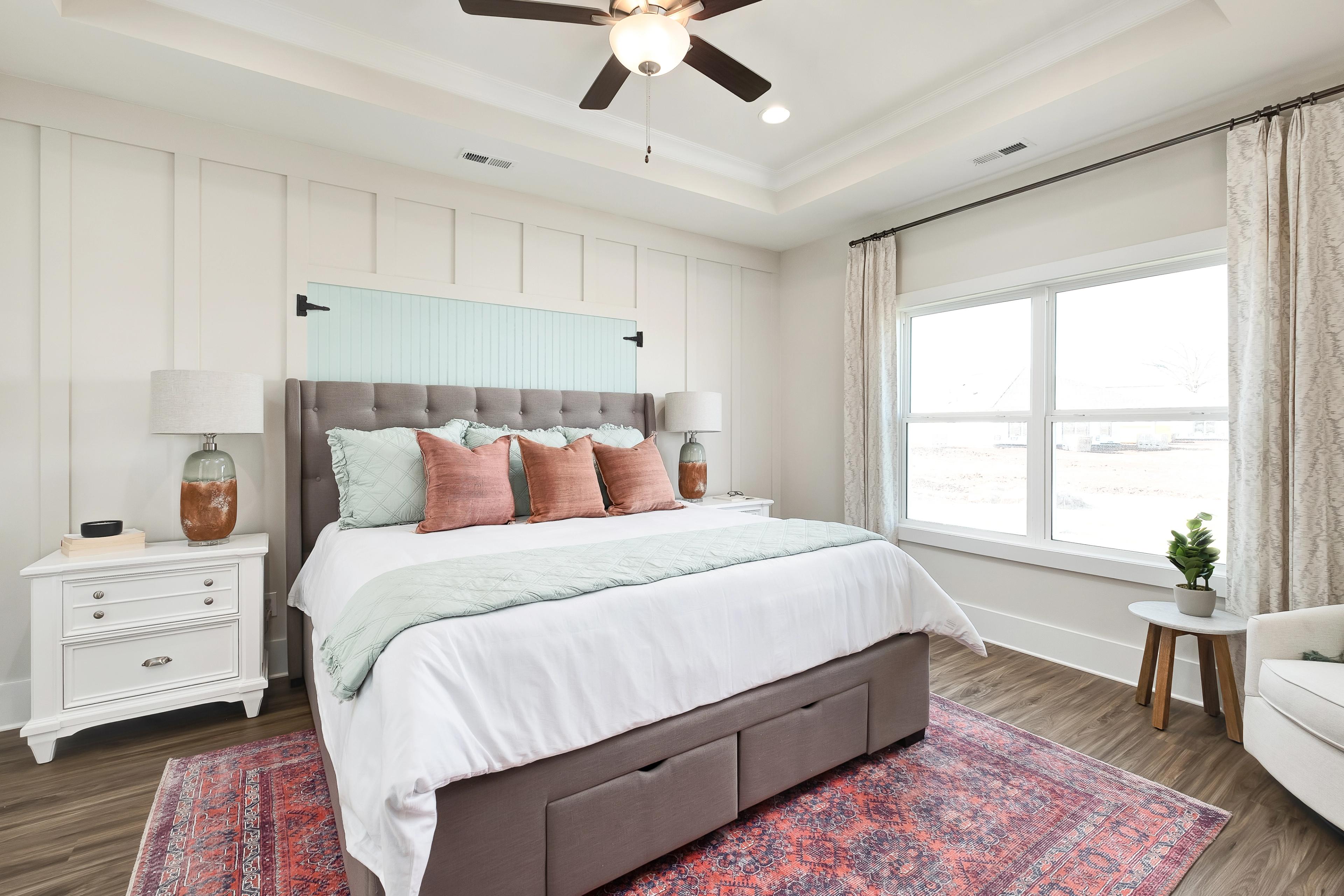 Cozy master bedroom at Mallard Landing in Athens Alabama featuring shiplap walls, tufted gray headboard bed, ceiling fan, and hardwood floors