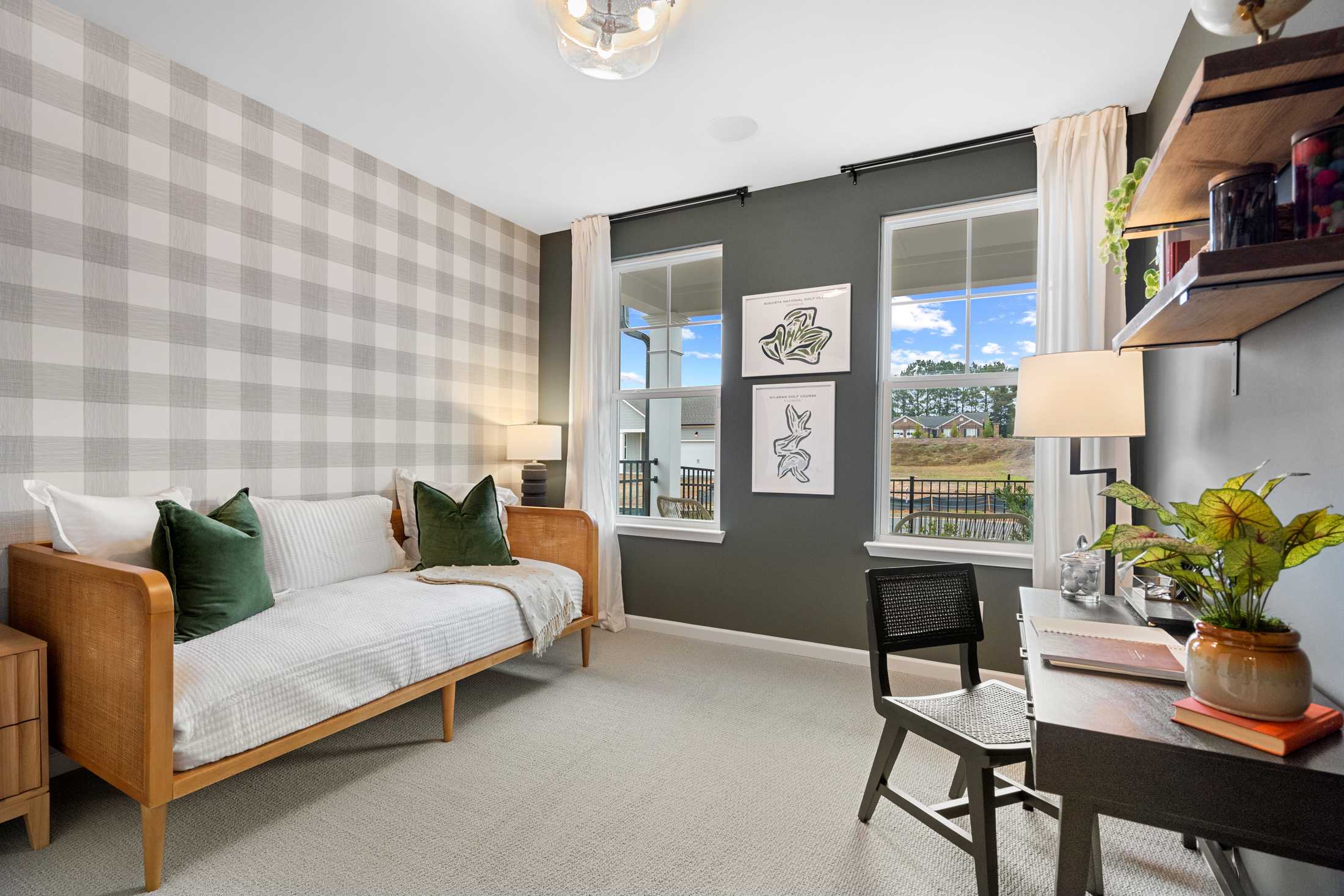 Cozy secondary bedroom in The Edison C by Davidson Homes, featuring gingham gray wallpaper, daybed with green pillows, wooden desk, and potted plants