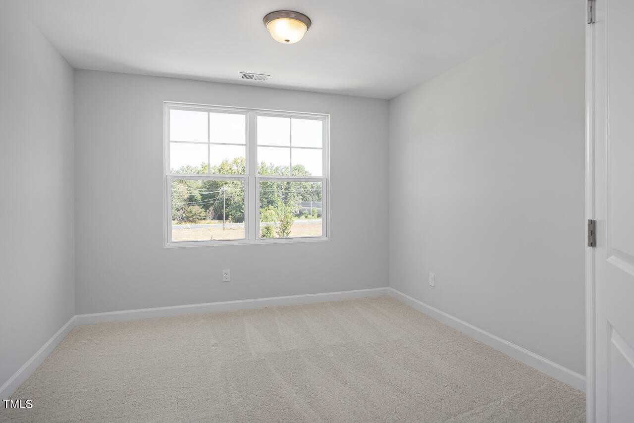Bright secondary bedroom with light gray walls, large window overlooking trees, beige carpet in Davidson Homes The Graham, Fuquay-Varina