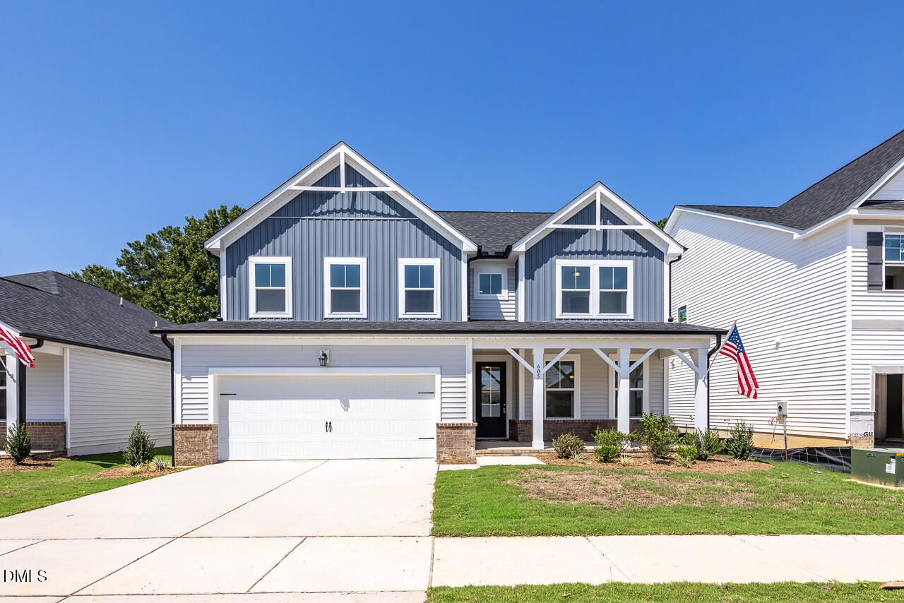 Two-story blue and white farmhouse-style exterior with covered porch and 2-car garage at Woodland Crossing, Zebulon, NC
