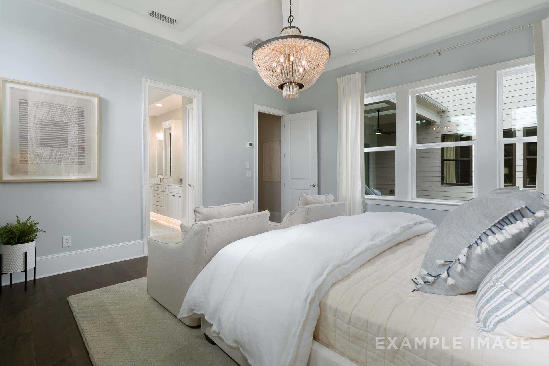 Spacious master bedroom in The Seaside with king bed, beaded chandelier, blue accents, and ensuite door