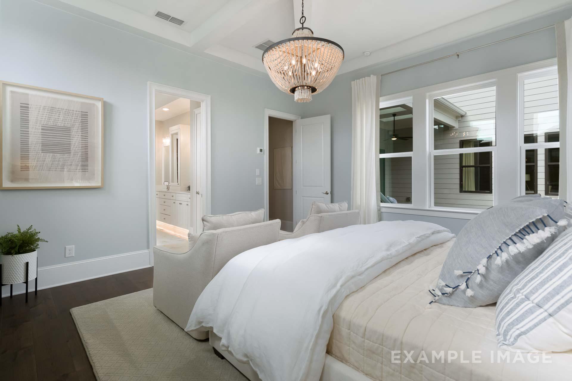 Serene master bedroom in The Seaside C with soft blue walls, chandelier, king bed, accent chairs, and large windows