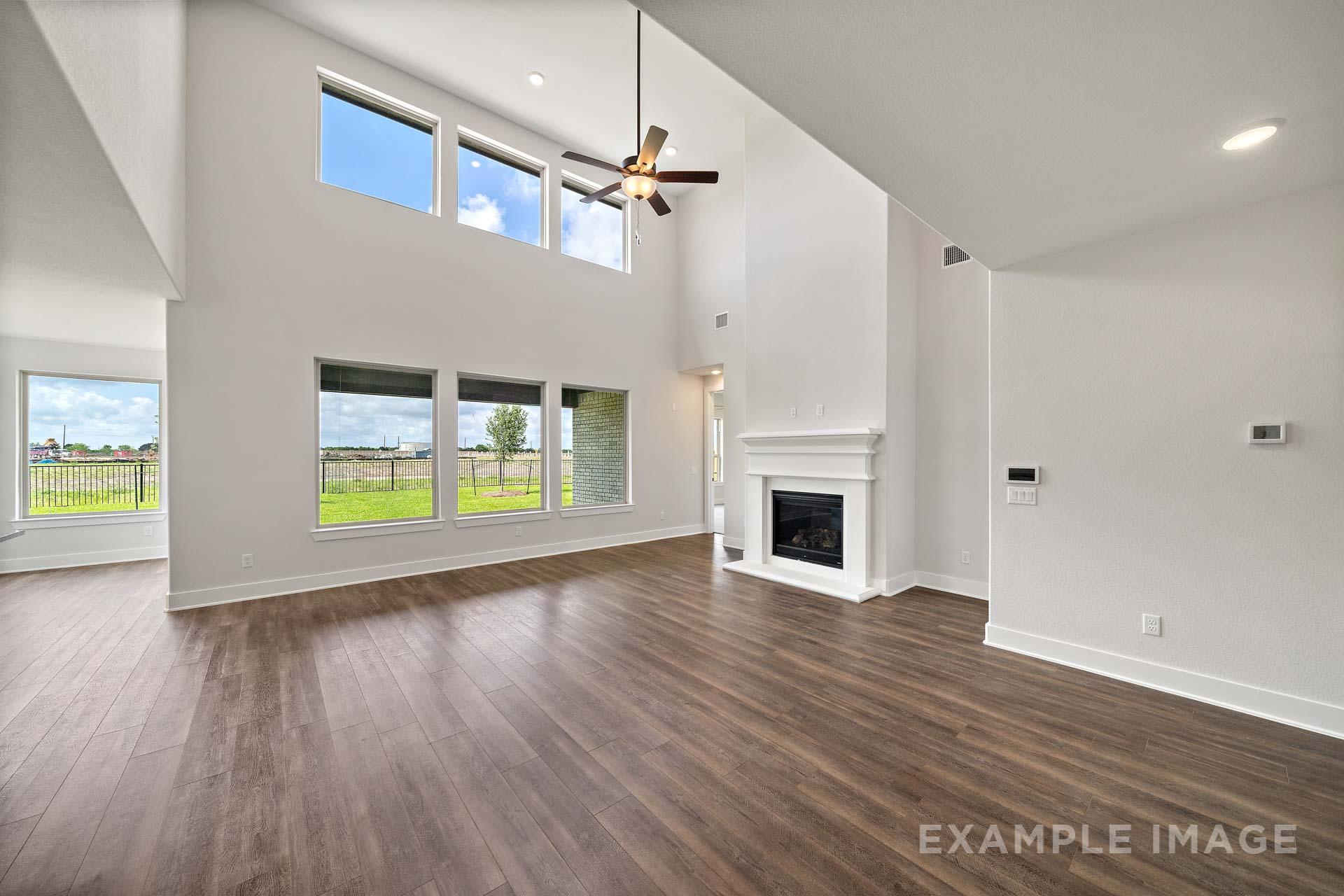 Spacious two-story living room in The Victoria A with vaulted ceilings, large windows, white stone fireplace, ceiling fan, and hardwood floors